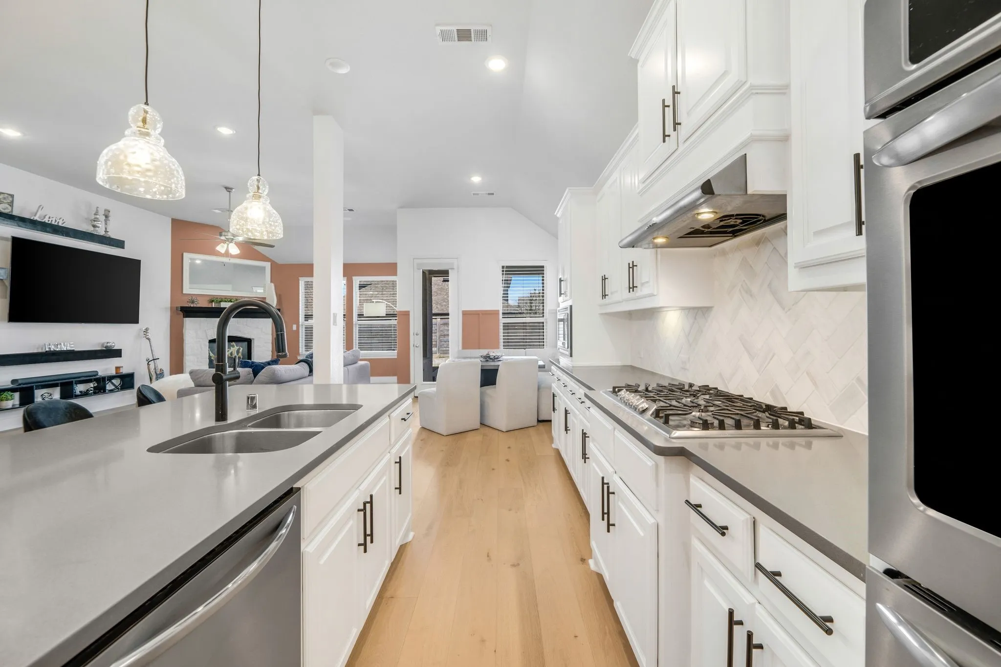 Kitchen featuring white shaker-style cabinetry, quartz countertops, herringbone-patterned tile backsplash, stainless steel gas cooktop, and wood-finish flooring