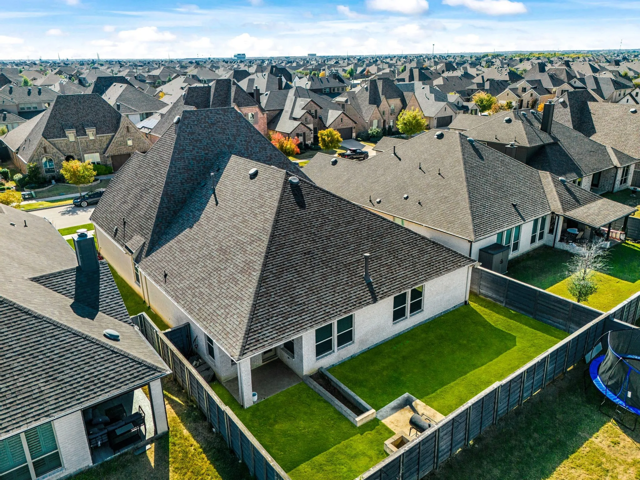 Aerial perspective showcasing a residential property featuring a backyard with a stone-surfaced patio, built-in raised masonry garden bed, and wood-style privacy fencing