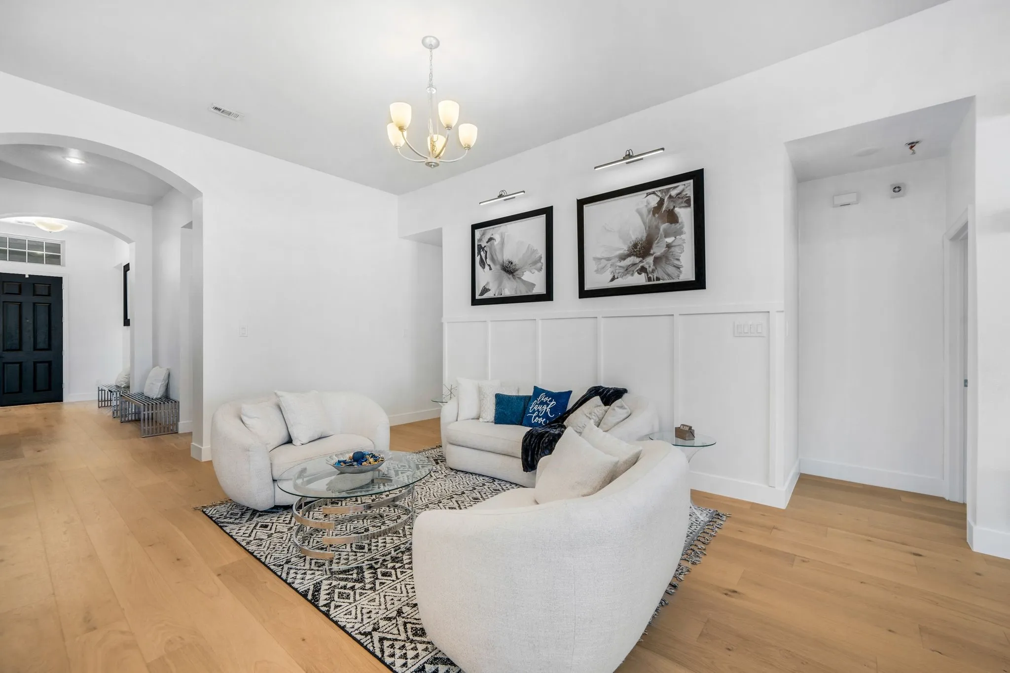 Living area featuring wood-finish flooring, architectural arched openings, wall-mounted picture lighting, board and batten wainscoting, and a multi-arm chandelier