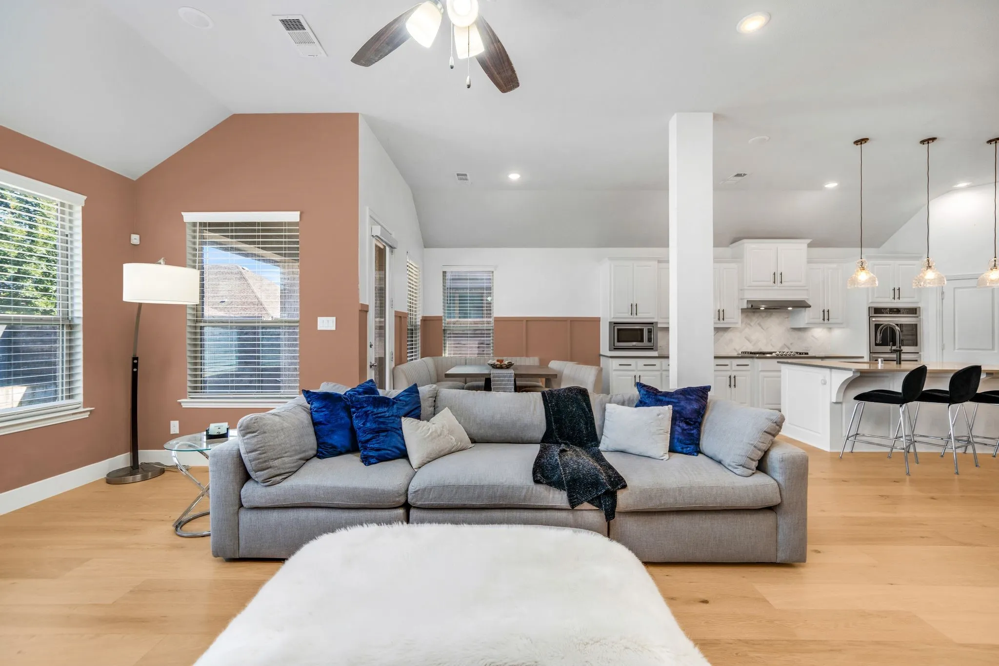 Vaulted ceilings, wood-finish flooring, recessed lighting, and kitchen featuring white cabinetry and a breakfast bar