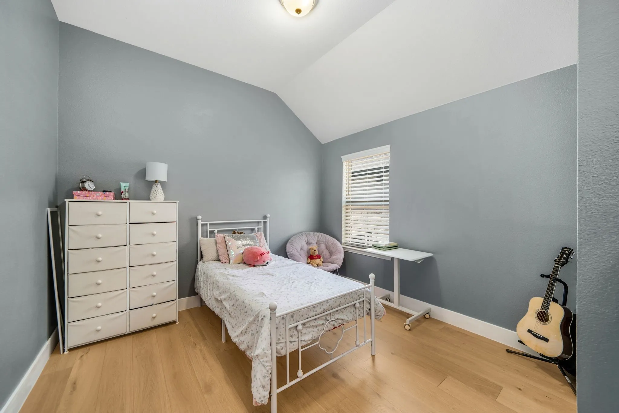 Vaulted ceiling, wood-finish flooring, and single-pane window with horizontal blinds