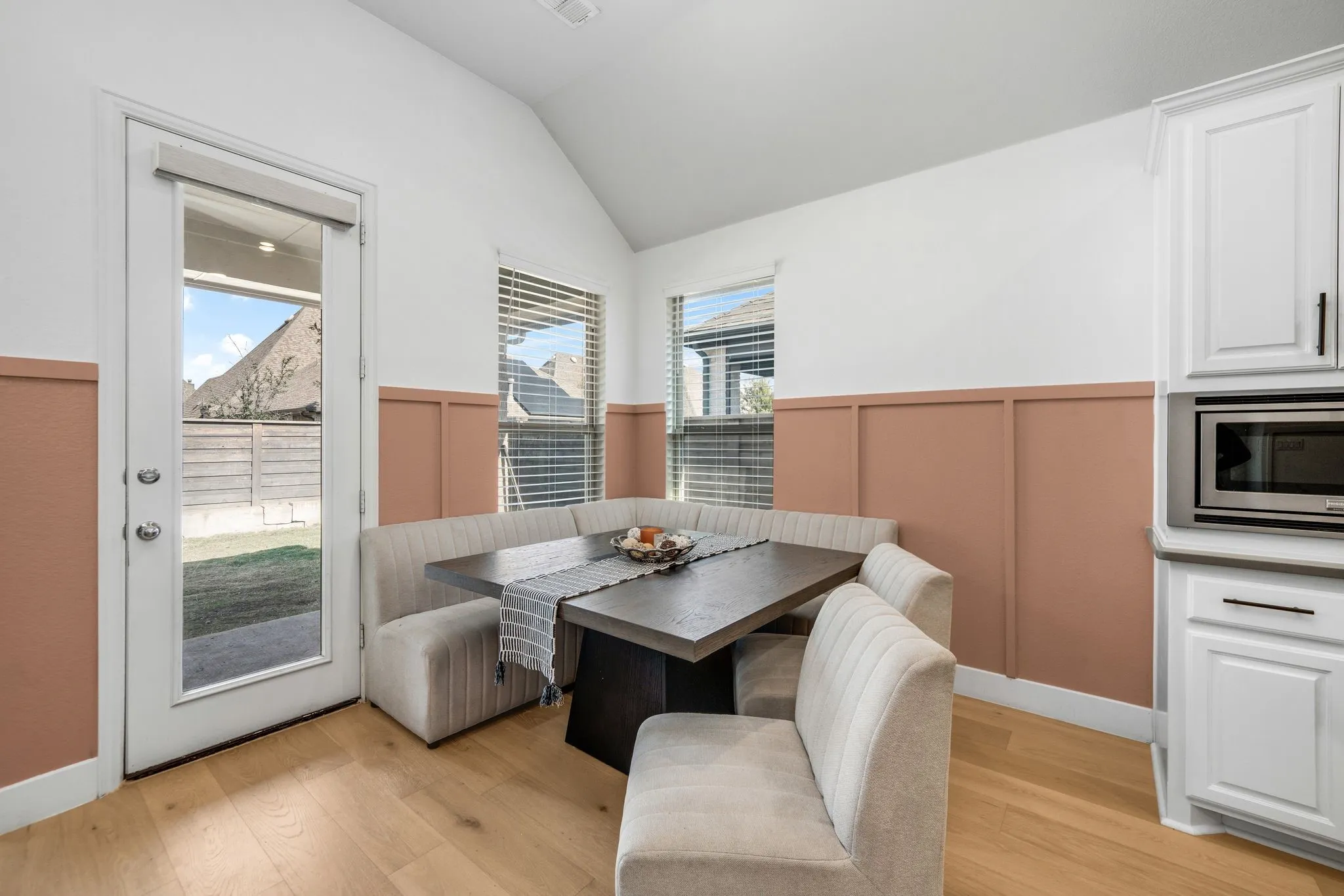 Vaulted ceiling with wood-finish flooring, half-wall board and batten wainscoting, white cabinetry with integrated microwave, and a glass-paneled exterior door