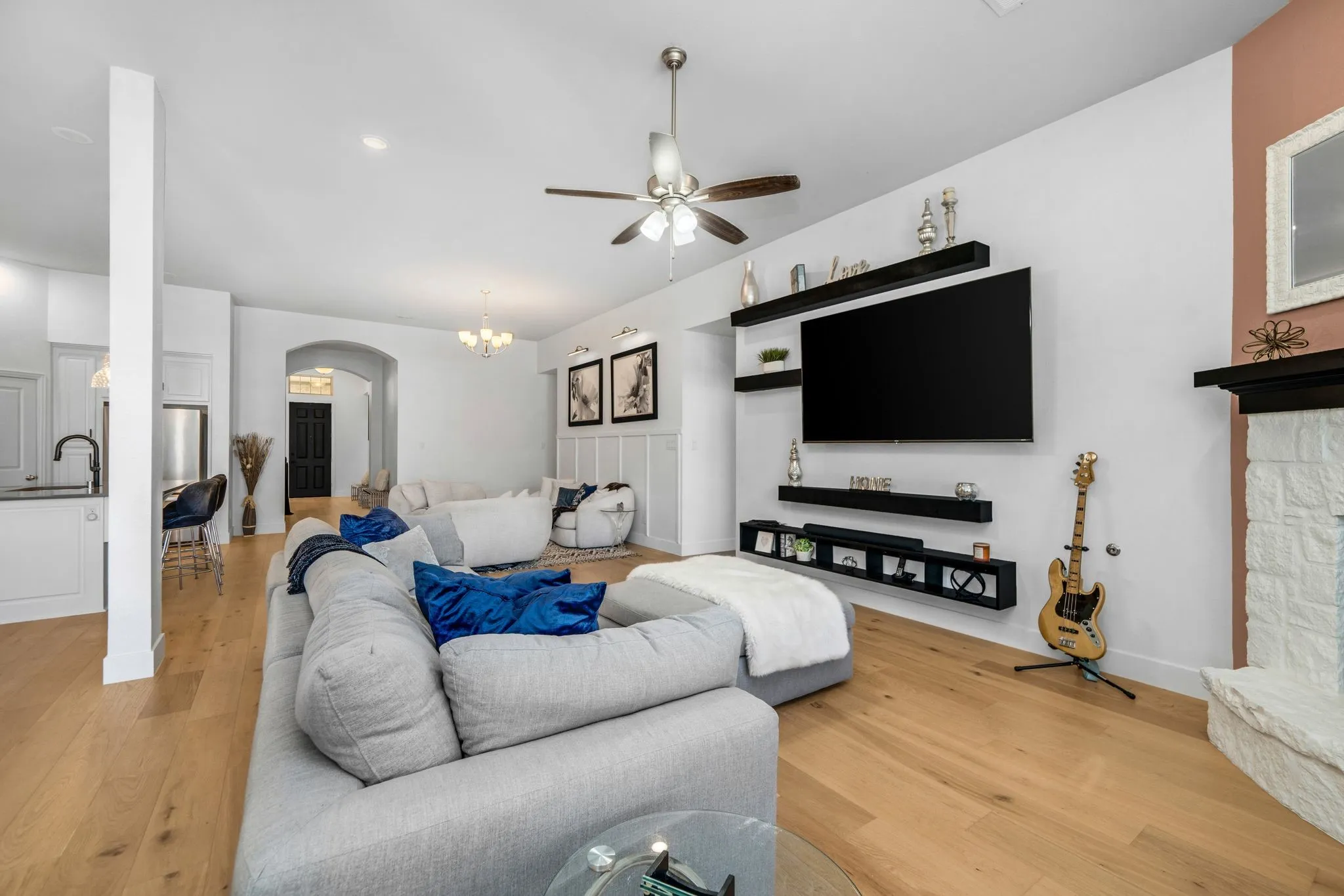 Living area featuring wood-finish flooring, a stone-faced fireplace with a mantel, integrated wall-mounted shelving, and a ceiling fan