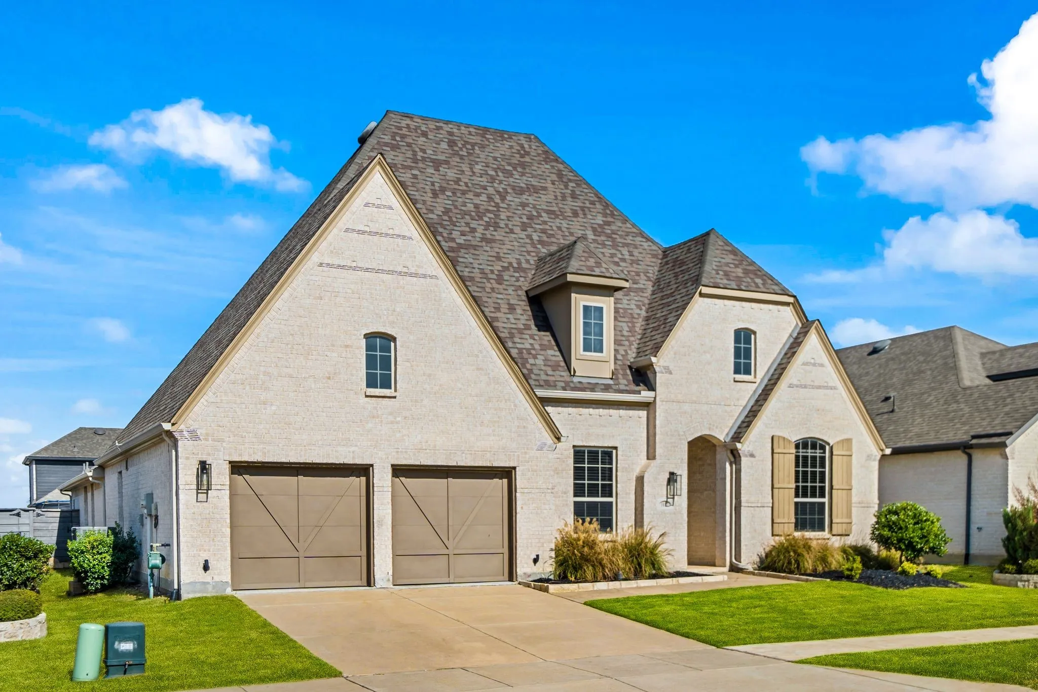 Traditional brick exterior featuring a steeply pitched roof, arched entryway, wooden shutters, and a two-car garage