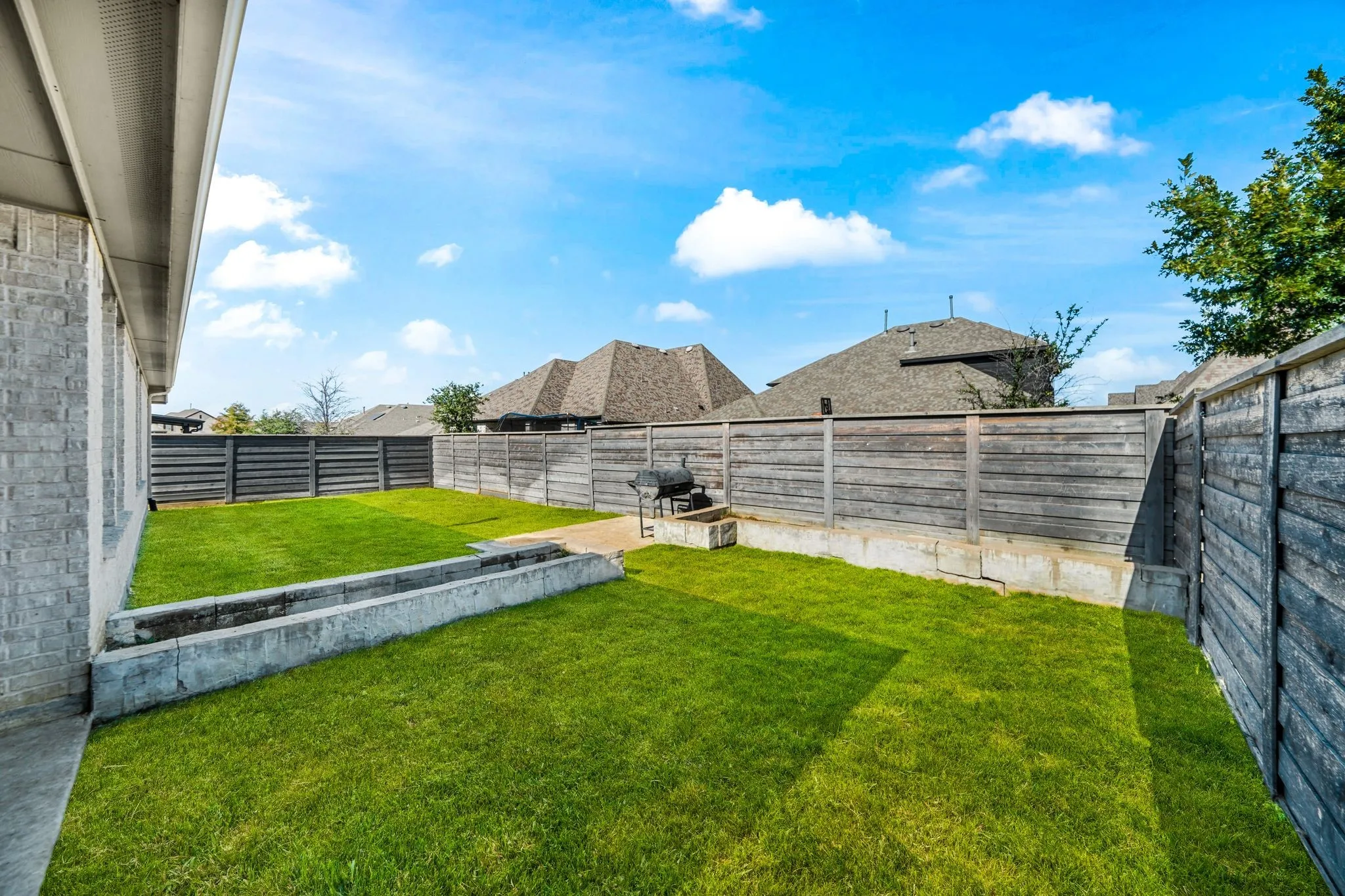 Private backyard featuring a manicured lawn, full-height wood fencing, and concrete raised garden beds