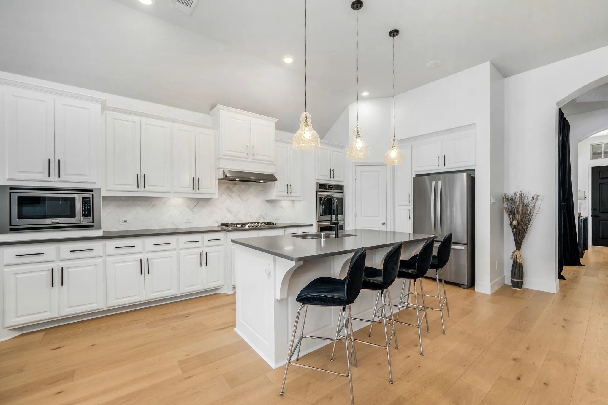 Kitchen featuring white shaker cabinetry, stainless steel appliances, a center island with a solid surface countertop, herringbone-patterned tile backsplash, and wood-finish flooring