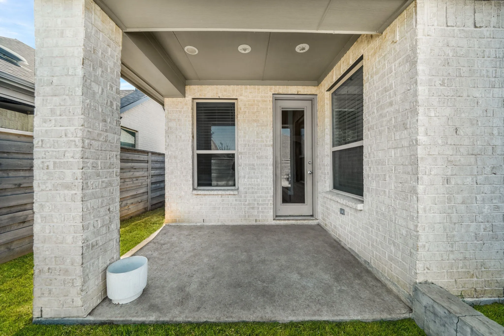 Covered concrete patio featuring white brick exterior walls, recessed ceiling lighting, and double-paned windows