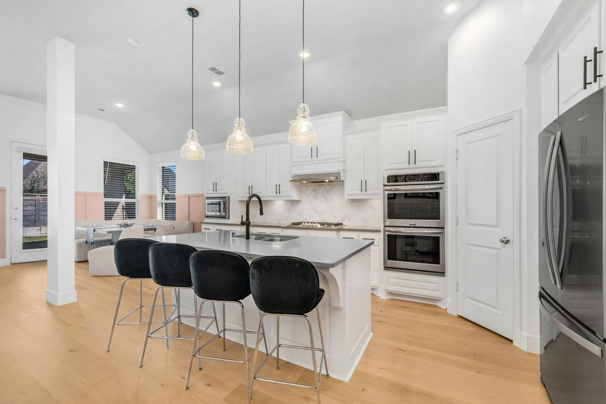 Kitchen featuring white shaker-style cabinetry, center island with stone countertop, herringbone tile backsplash, stainless steel double wall ovens, and wood-finish flooring