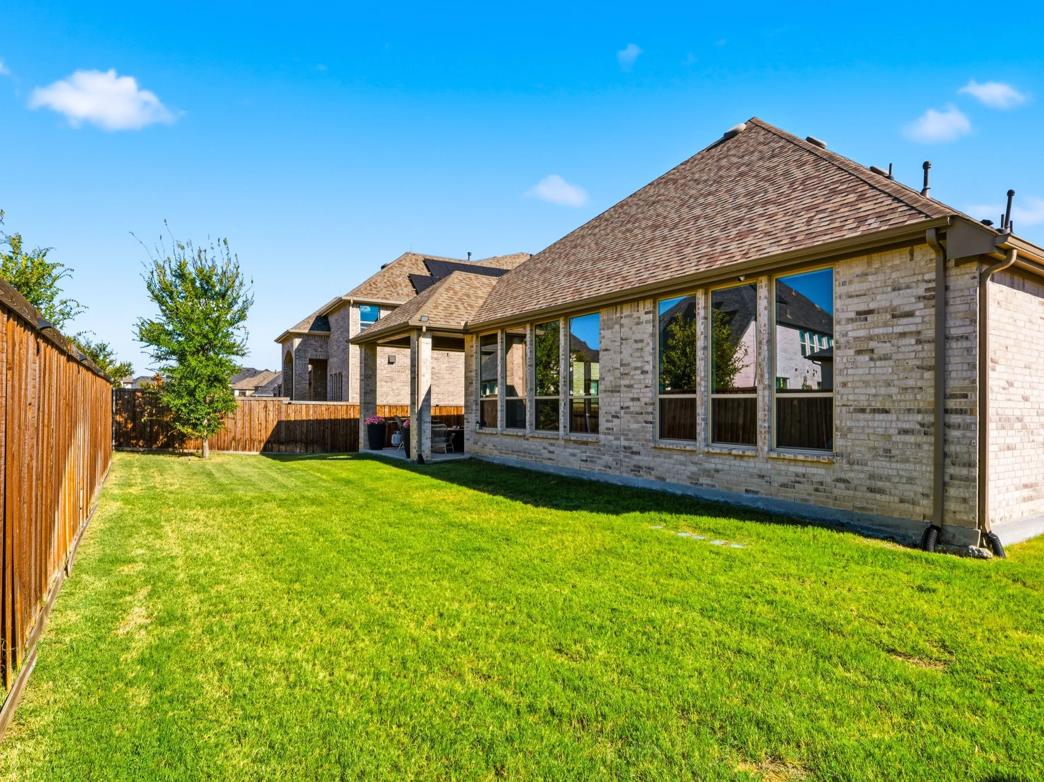 Backyard featuring a masonry exterior, multi-pitched shingle roof, covered patio, and wood privacy fencing