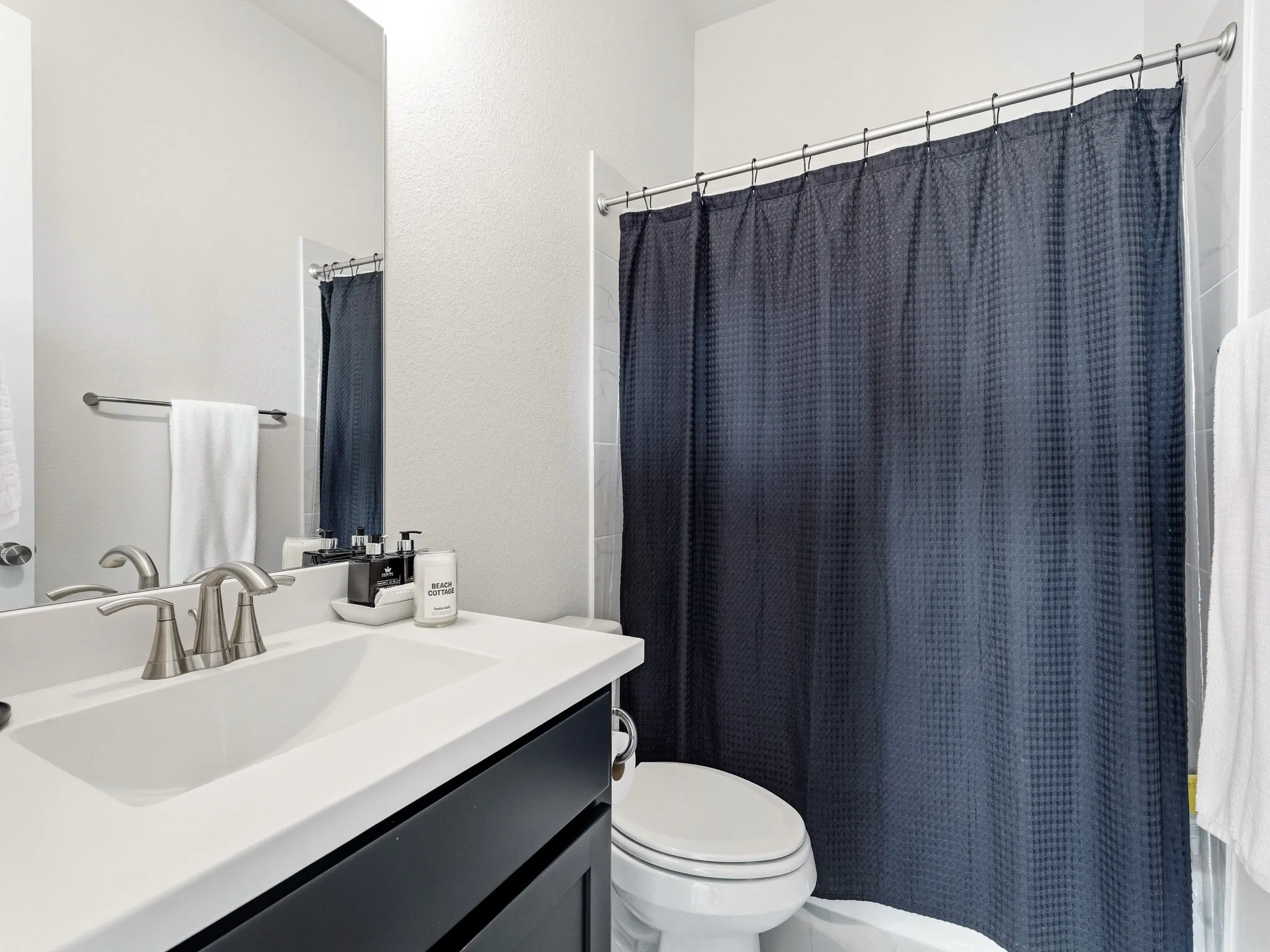 Bathroom featuring a dark wood-finish vanity, white countertop with an integrated basin, brushed nickel faucet, large wall mirror, and a tub-shower combination with tiled surround