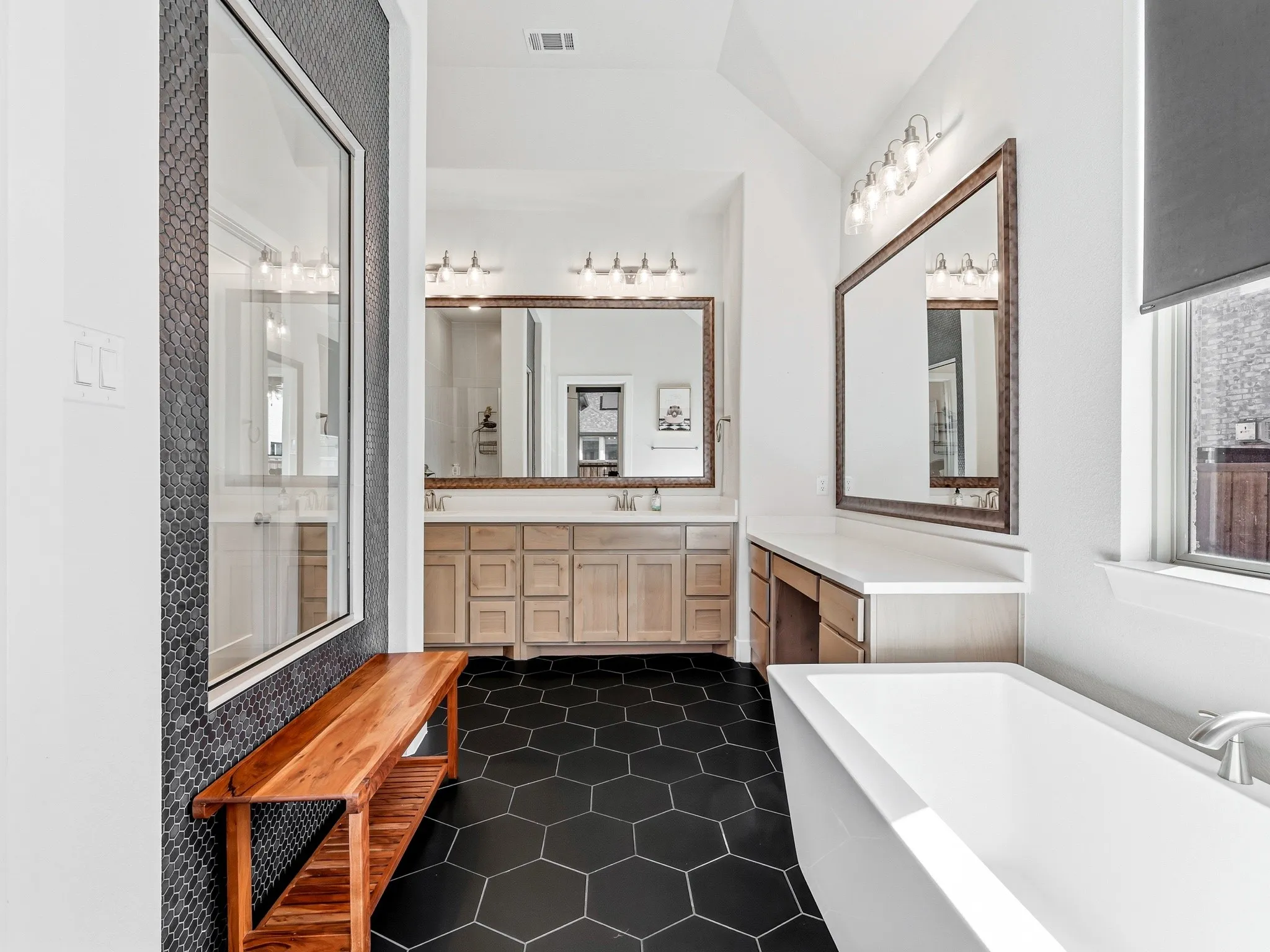 Bathroom featuring matte black hexagonal floor tile, a freestanding soaking tub, dual-sink vanity with wood-finish cabinetry, and a dark circular-tile accent wall