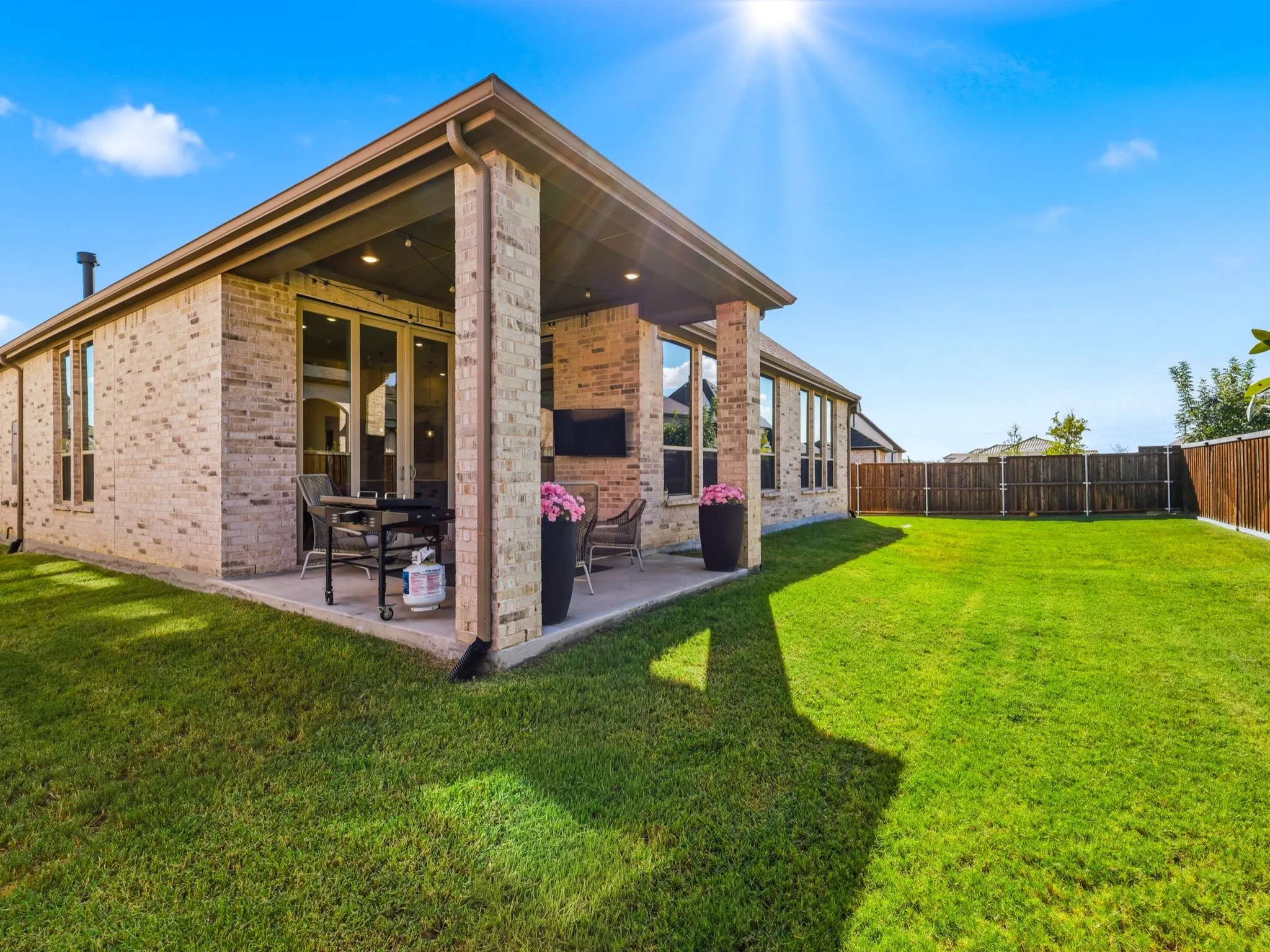Covered rear patio with recessed lighting, brick exterior, and expansive grass lawn enclosed by a wood privacy fence
