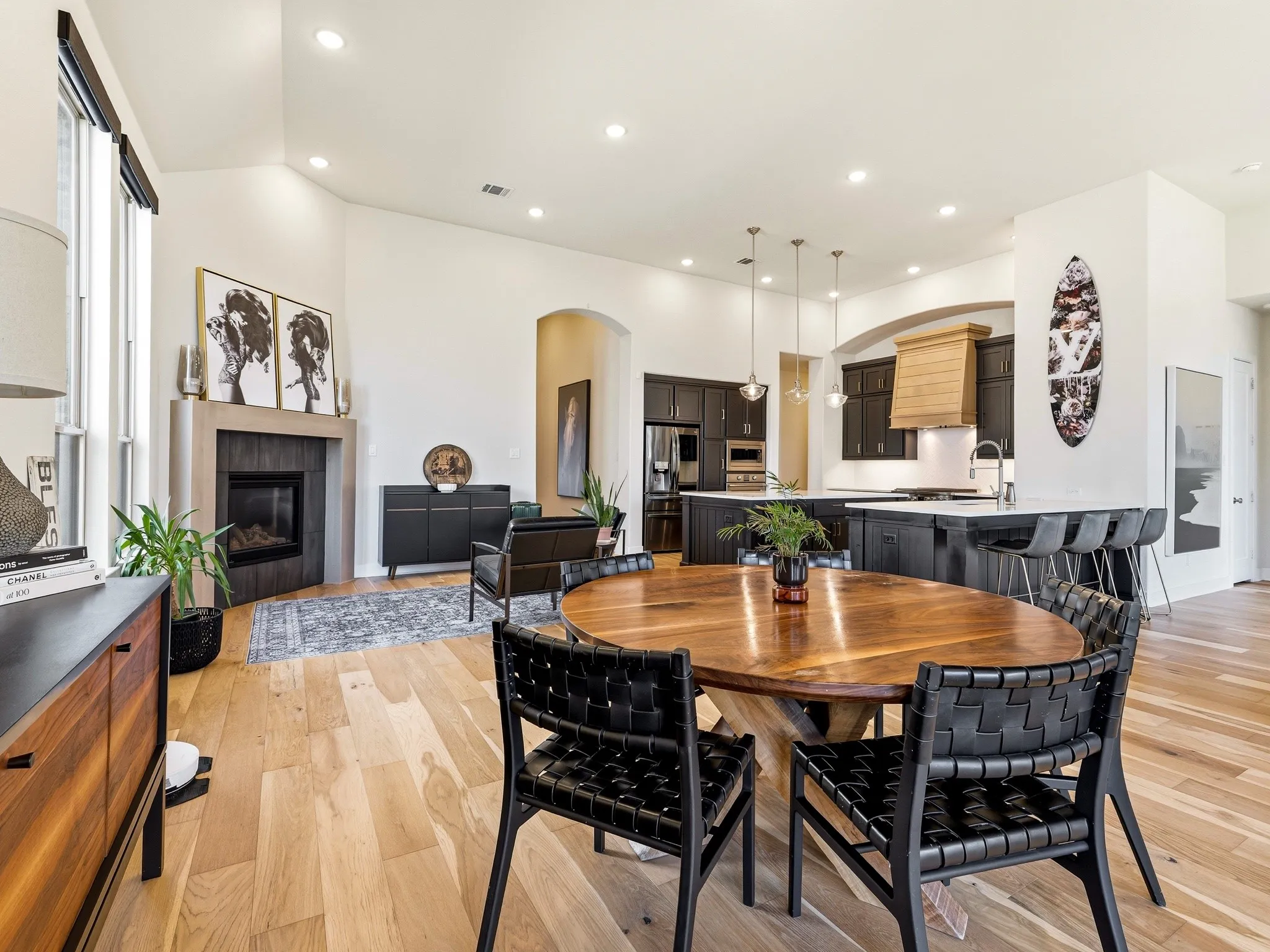 Open-concept interior featuring vaulted ceilings, wood-finish flooring, a stone-surround fireplace, dark cabinetry, and a large central kitchen island
