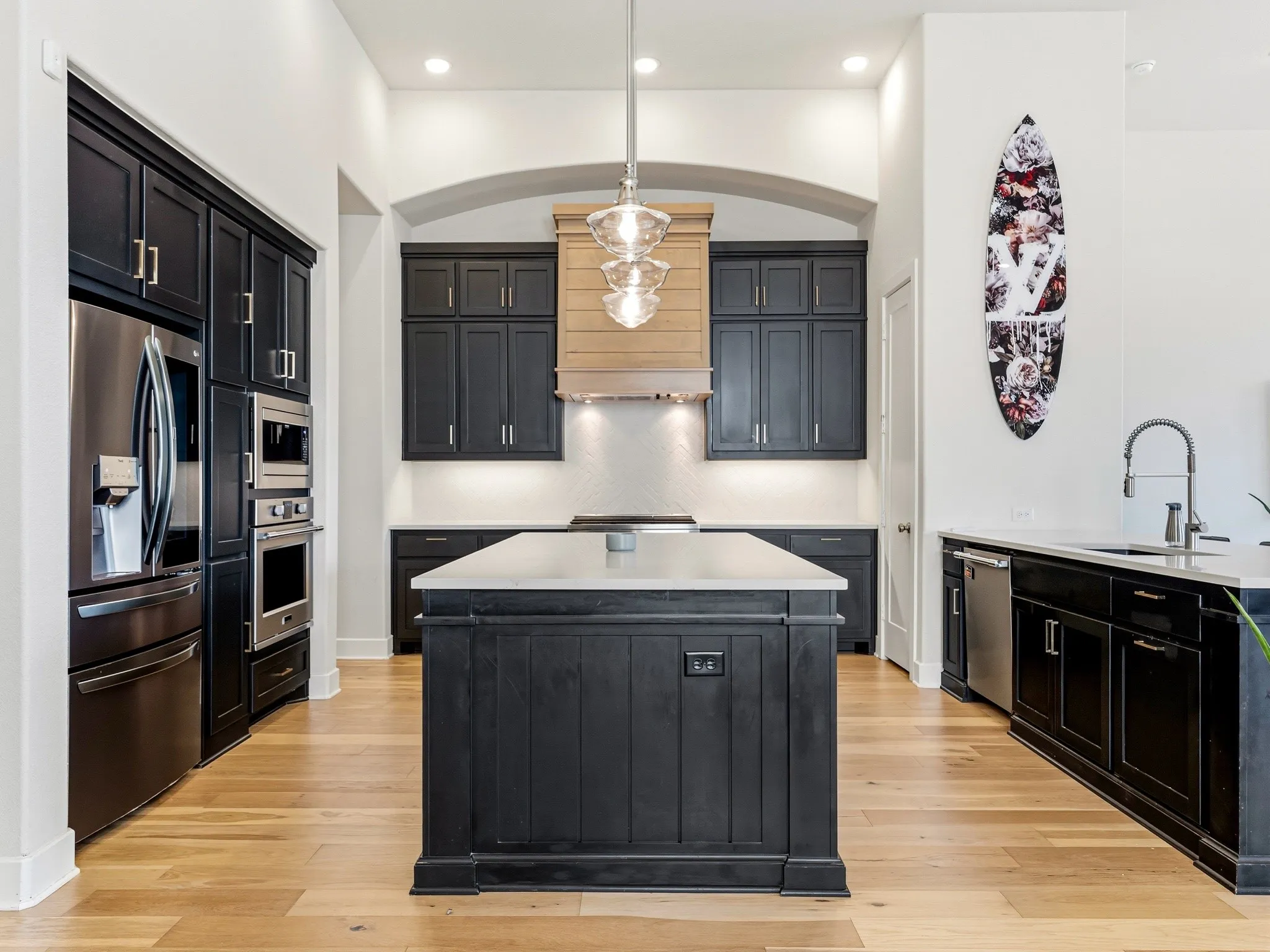 Kitchen featuring dark cabinetry, a central island with a light-toned countertop, wood-finish flooring, a wood-paneled range hood, and recessed lighting