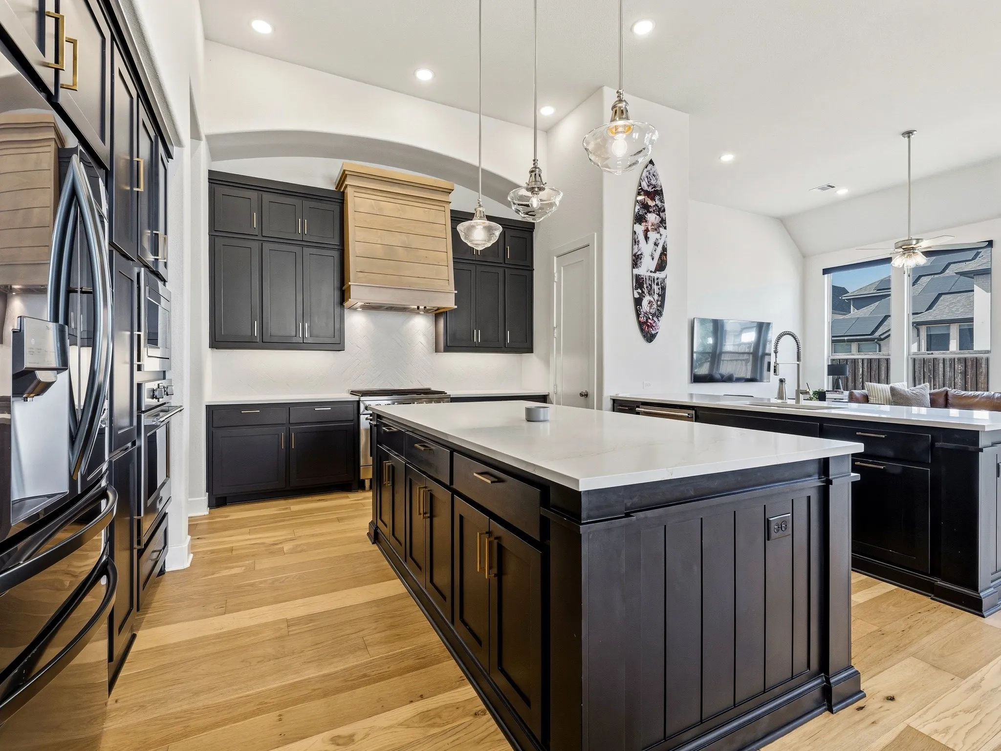 Kitchen featuring a central island with a solid surface countertop, custom dark cabinetry, wood-finish flooring, a wood-paneled range hood, and pendant lighting