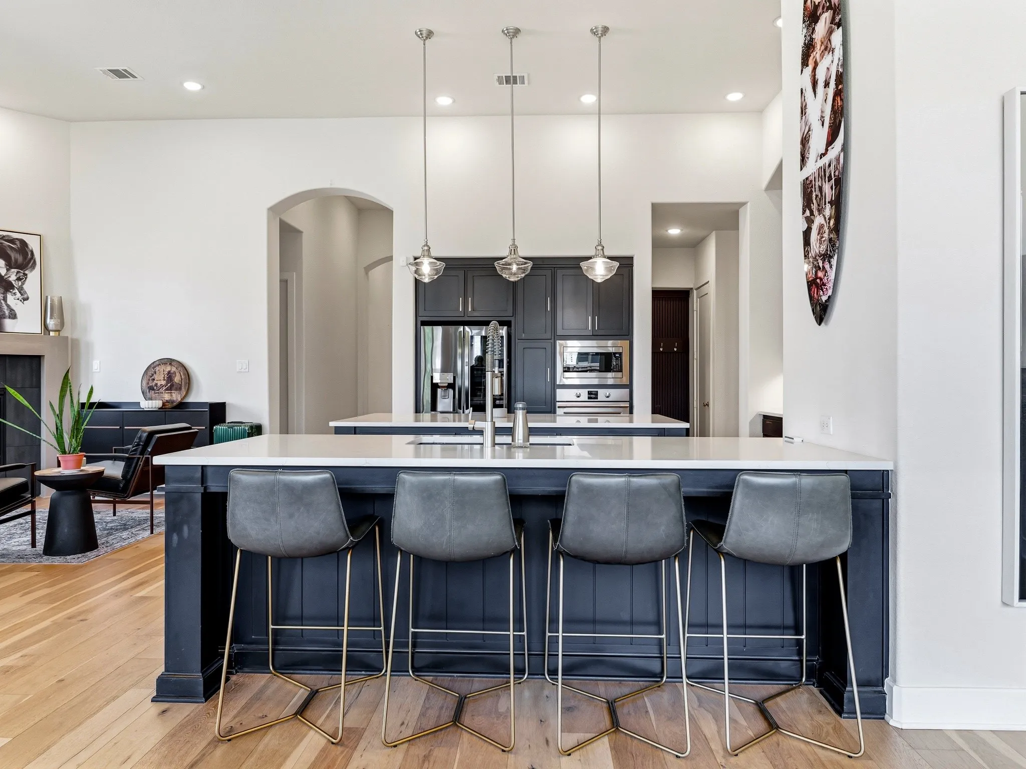 Kitchen featuring a central island with a quartz countertop, dark-toned cabinetry, three suspended pendant lights, and wood-finish flooring