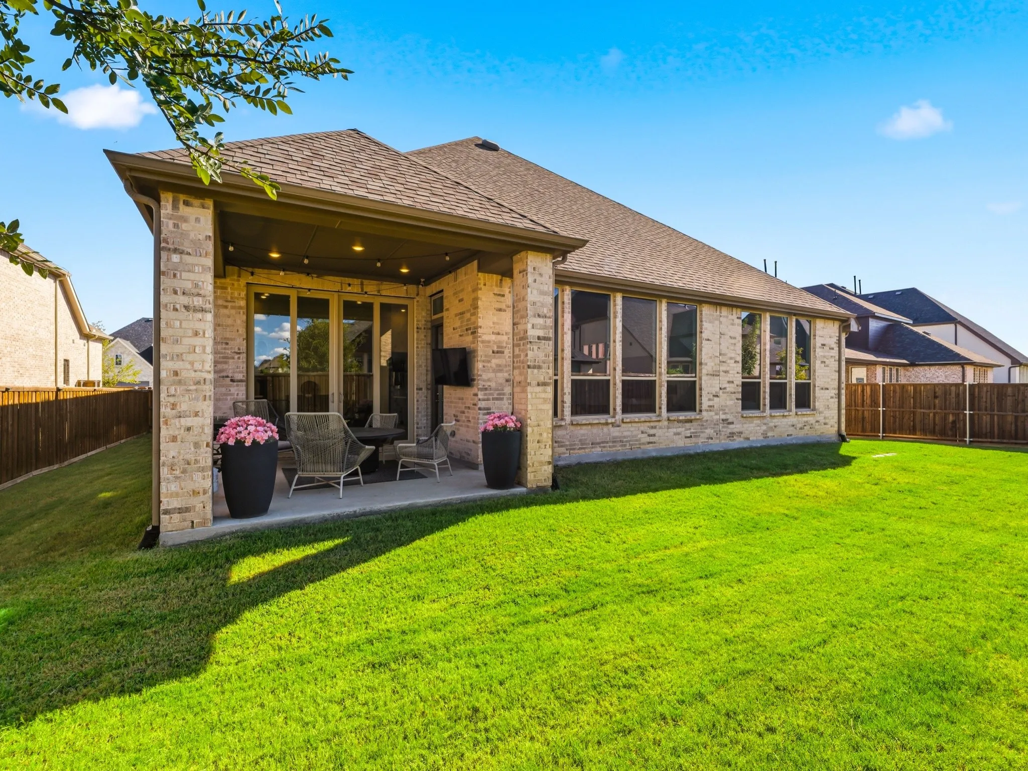 Brick exterior with covered concrete patio, recessed lighting, and expansive lawn enclosed by wood fencing