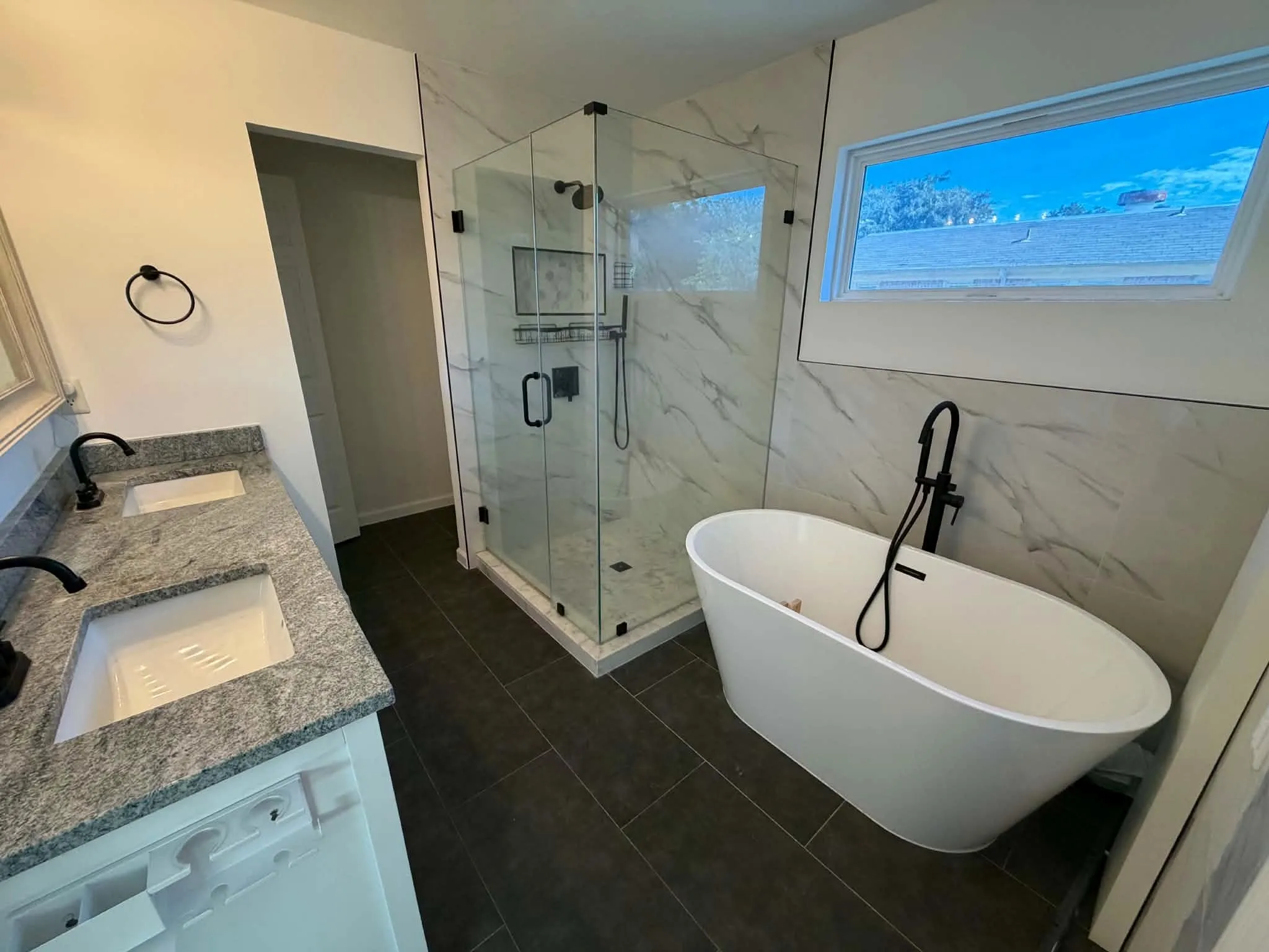 Bathroom featuring a dual-sink vanity with stone countertops, a standalone soaking tub with matte black fixtures, and a glass-enclosed walk-in shower with tile wall surround