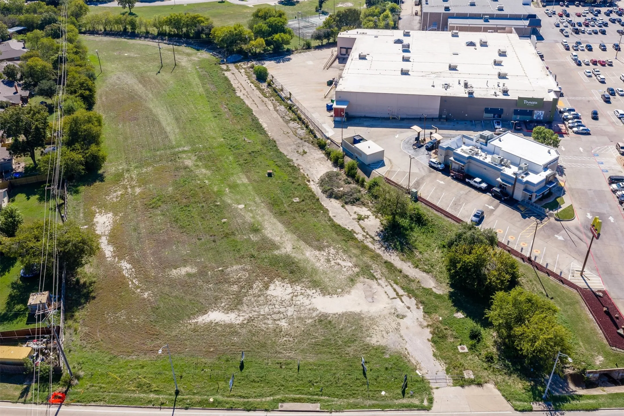 Expansive, undeveloped parcel of land featuring mature trees along the perimeter and frontage along a paved thoroughfare