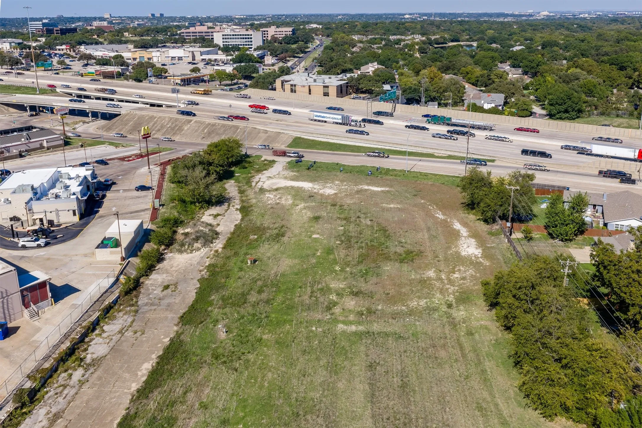 Undeveloped parcel featuring cleared land, mature trees, and direct frontage to major thoroughfare infrastructure
