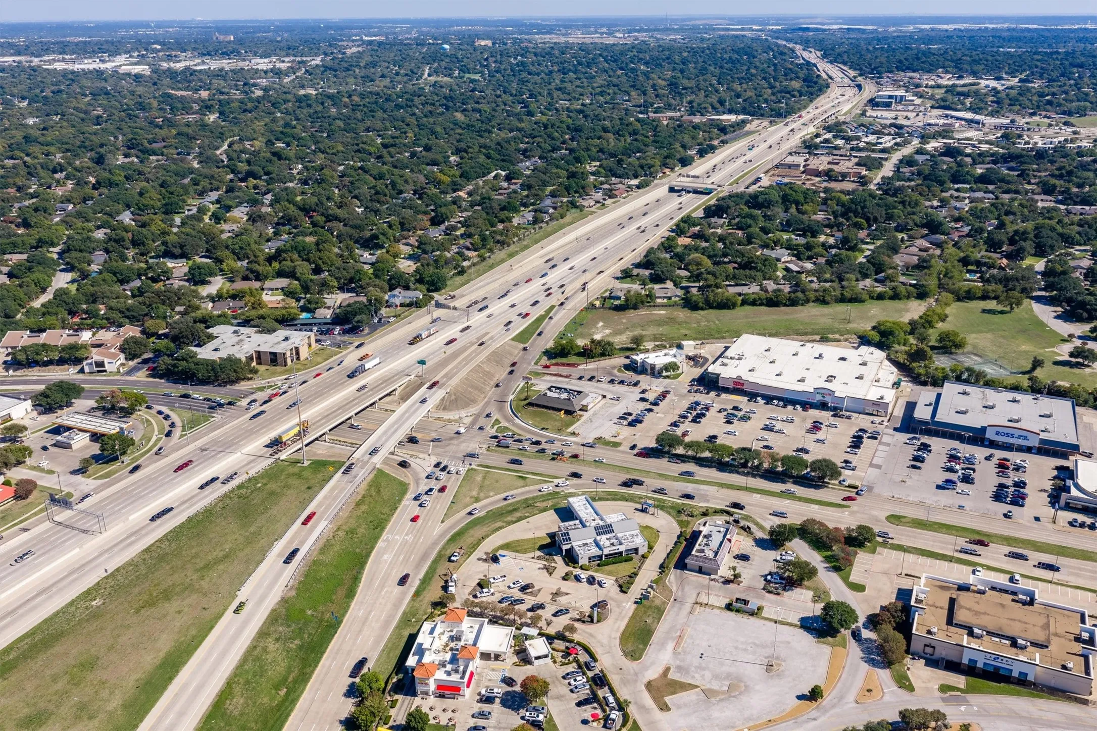 Aerial perspective of regional infrastructure featuring major highway access, commercial hubs, expansive parking facilities, and surrounding wooded landscapes