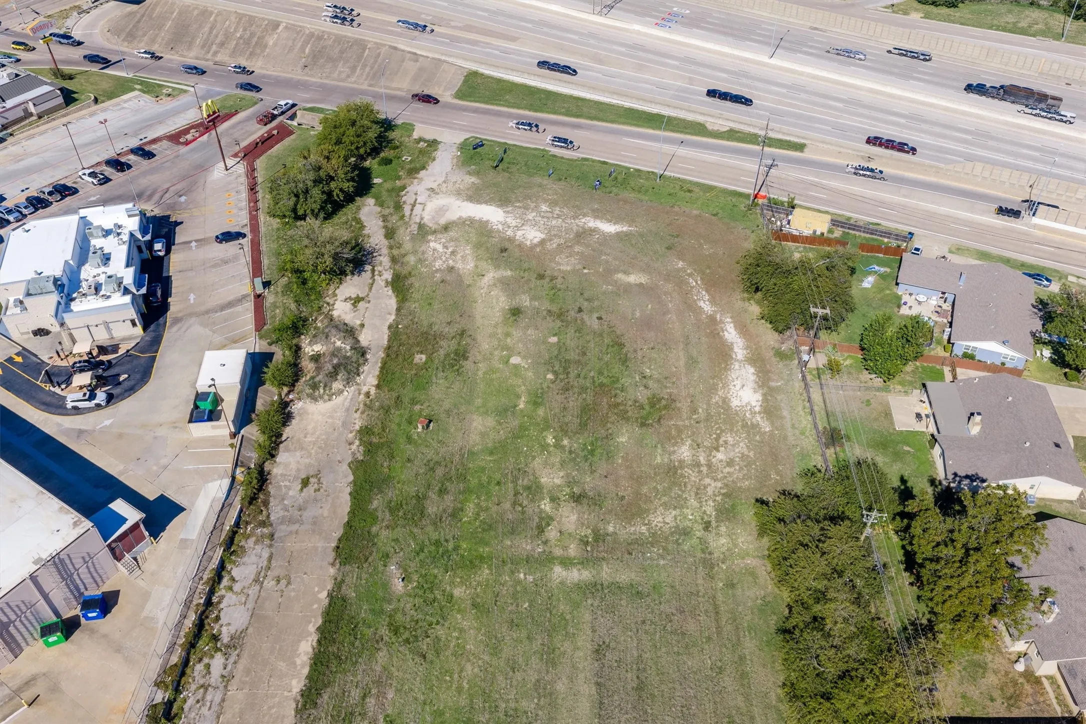 Vacant land parcel featuring expansive open terrain, established perimeter vegetation, and direct frontage to a major thoroughfare