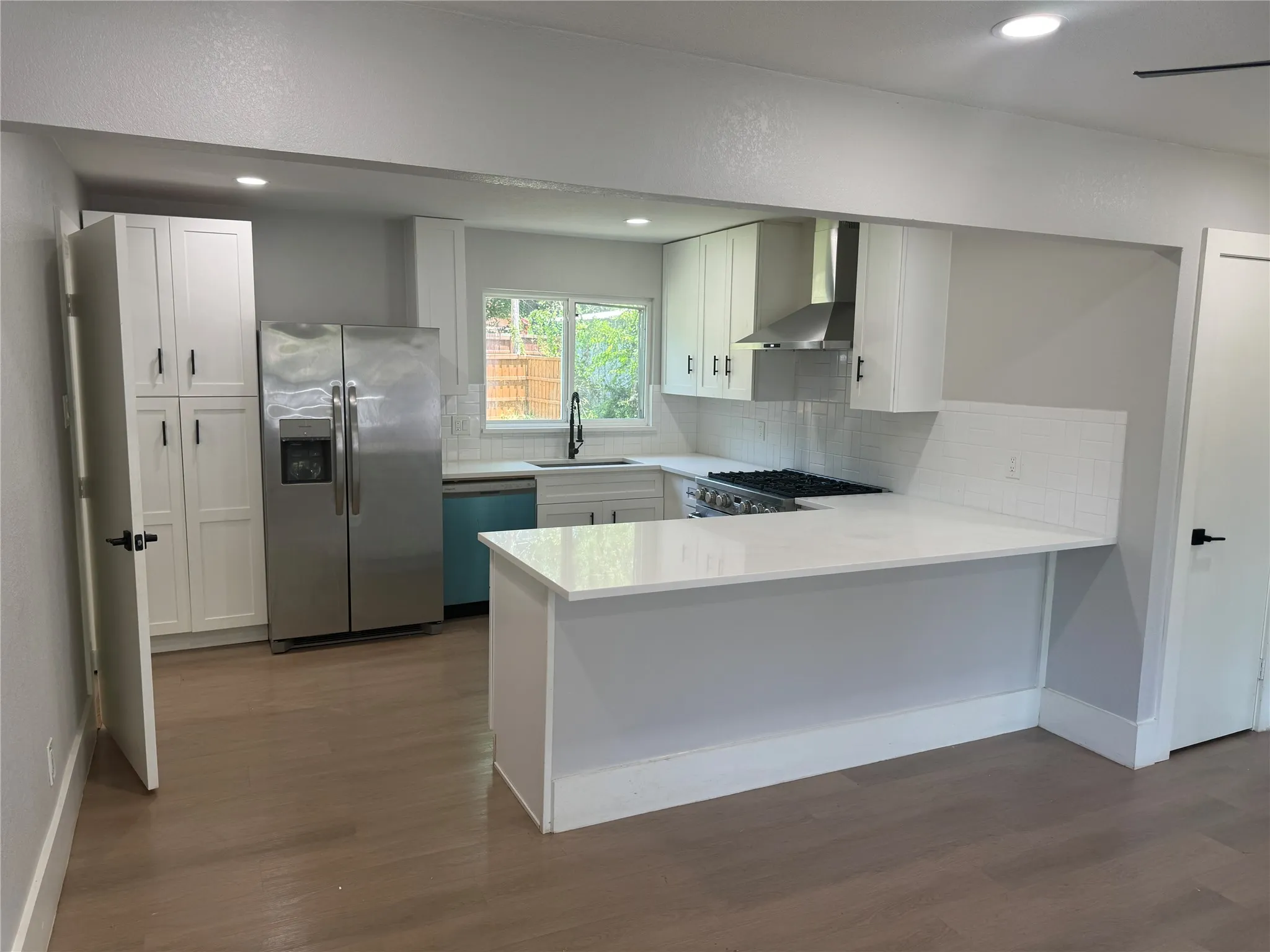 Kitchen featuring white shaker-style cabinetry, quartz countertops, stainless steel appliances, a subway tile backsplash, and wood-finish flooring