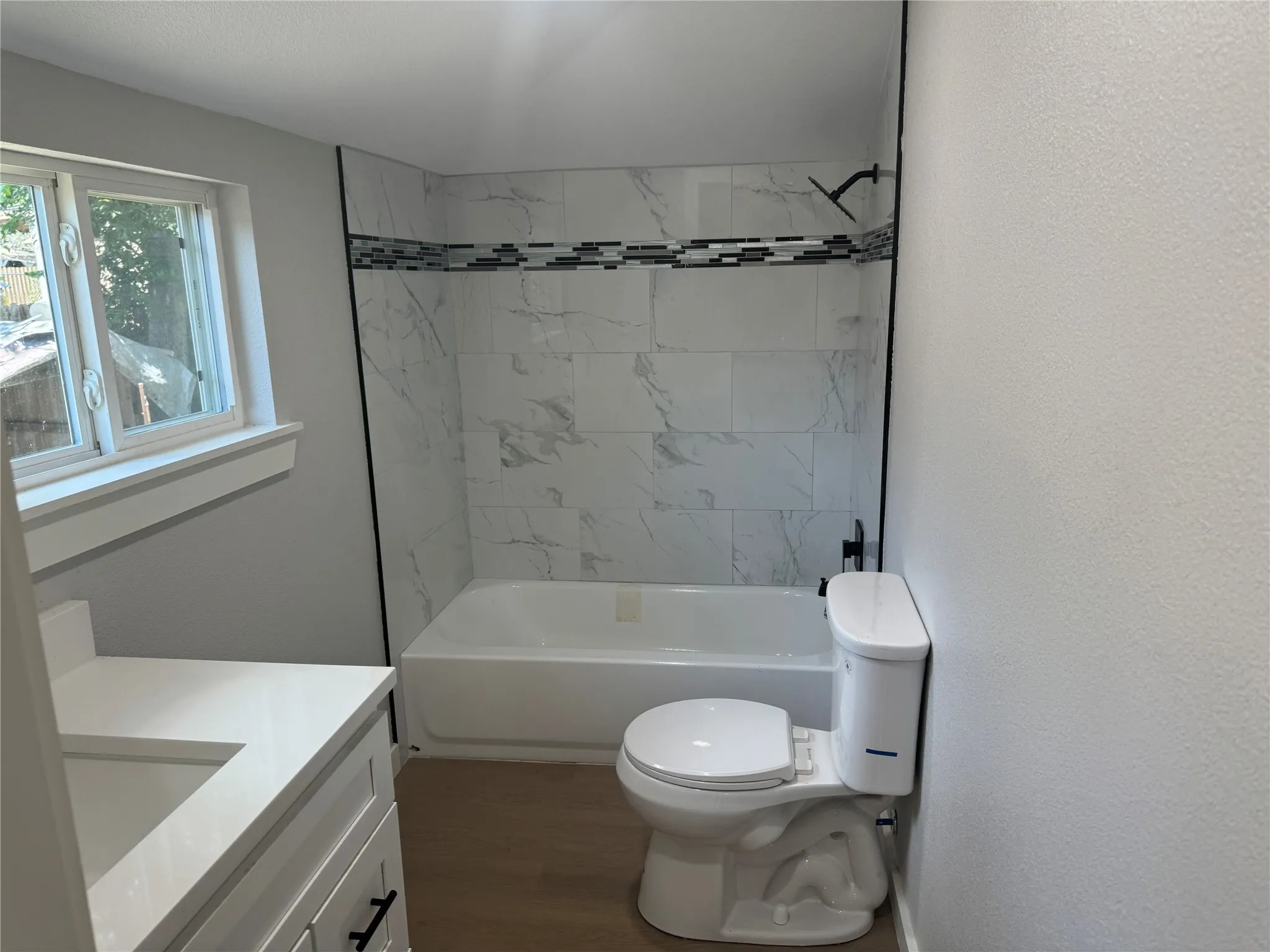 Bathroom featuring a white vanity with an integrated countertop, tub-shower combination with large-format wall tile, decorative mosaic tile inlay, and wood-finish flooring