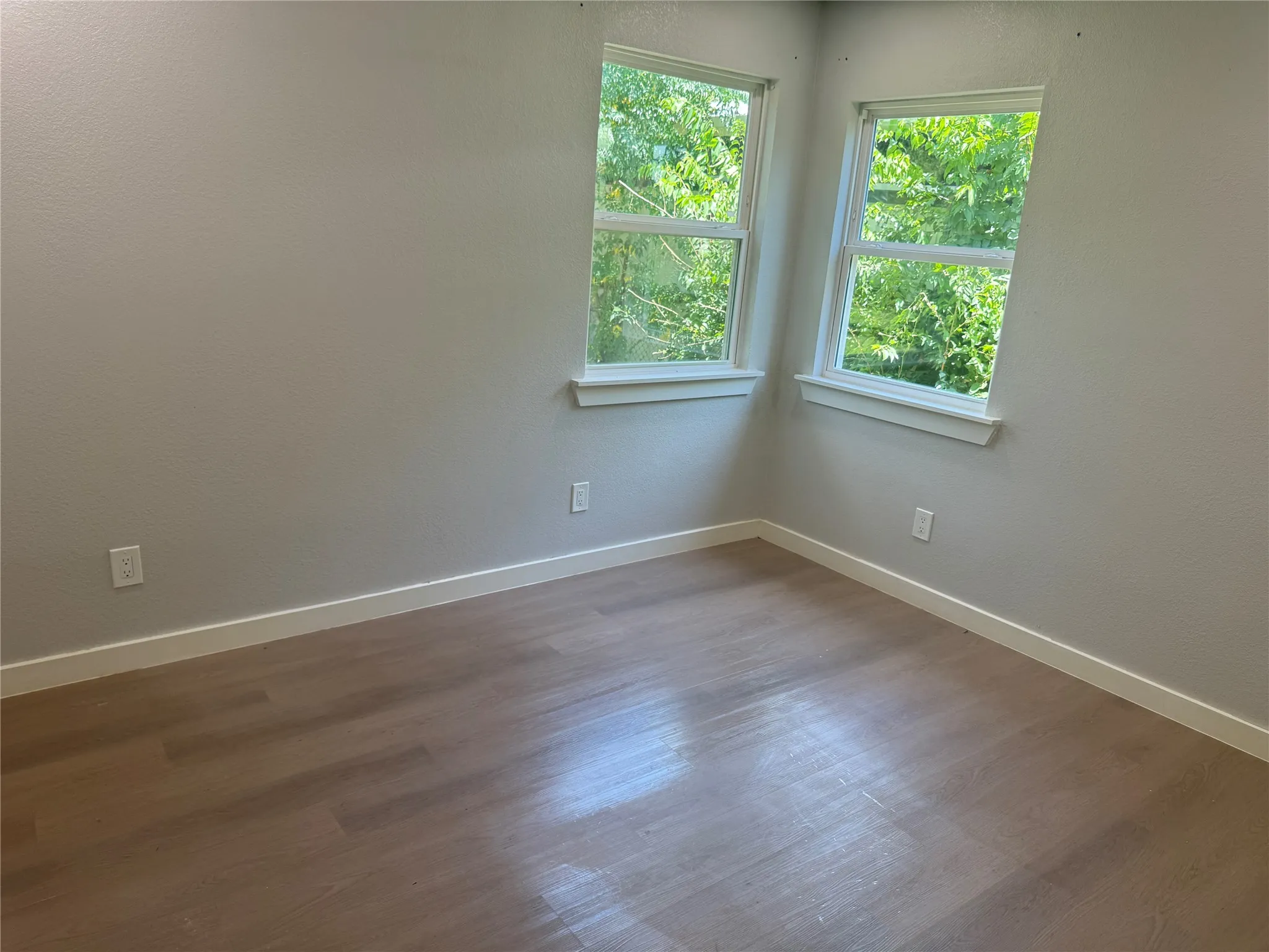 Room featuring neutral-toned walls, wood-finish flooring, and two windows with exterior natural greenery
