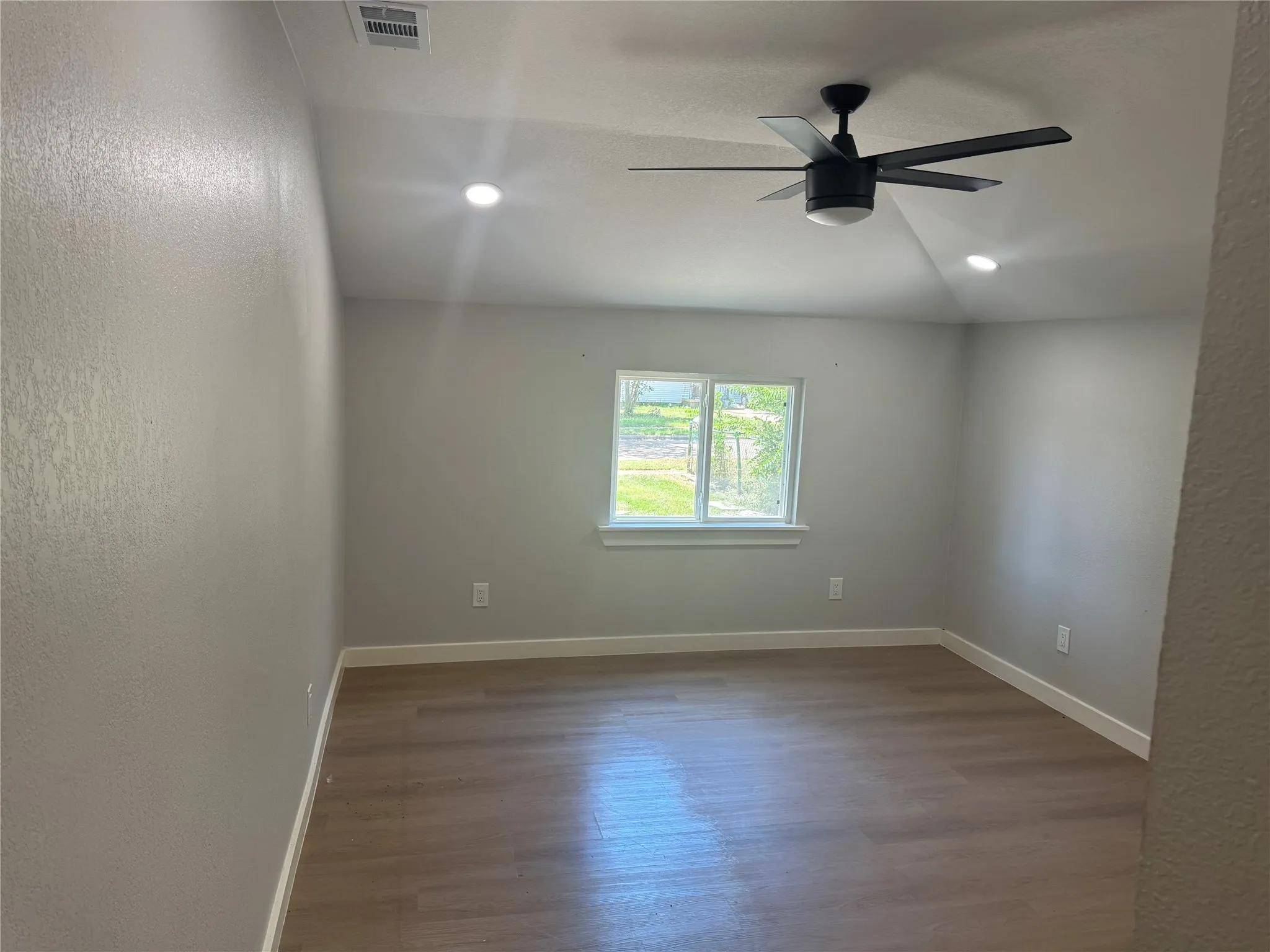 Room featuring a vaulted ceiling, wood-finish flooring, recessed lighting, and a matte black ceiling fan