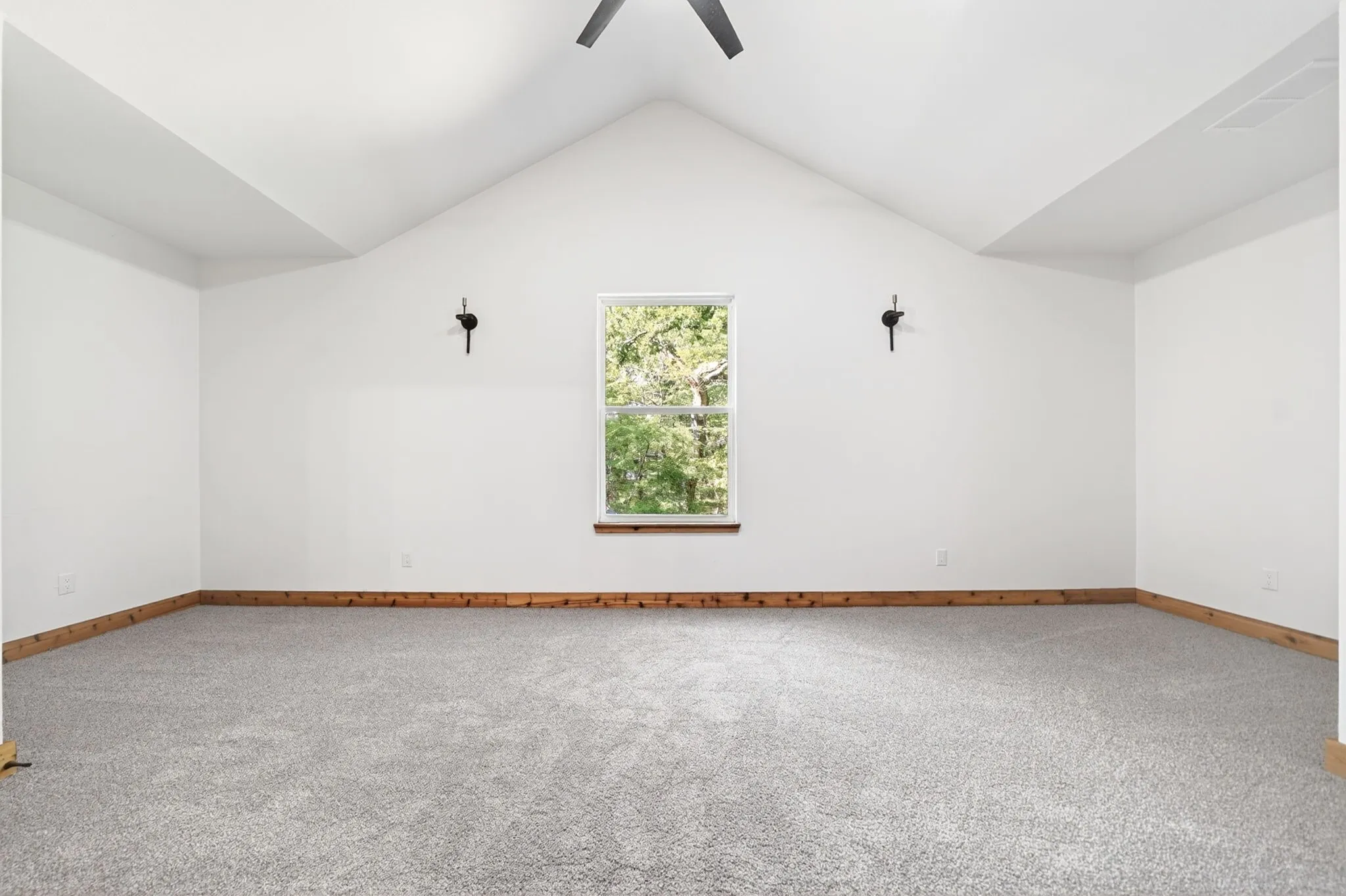 Vaulted ceiling featuring a central ceiling fan, neutral wall-to-wall carpeting, wood trim detailing, and dual wall-mounted light fixtures
