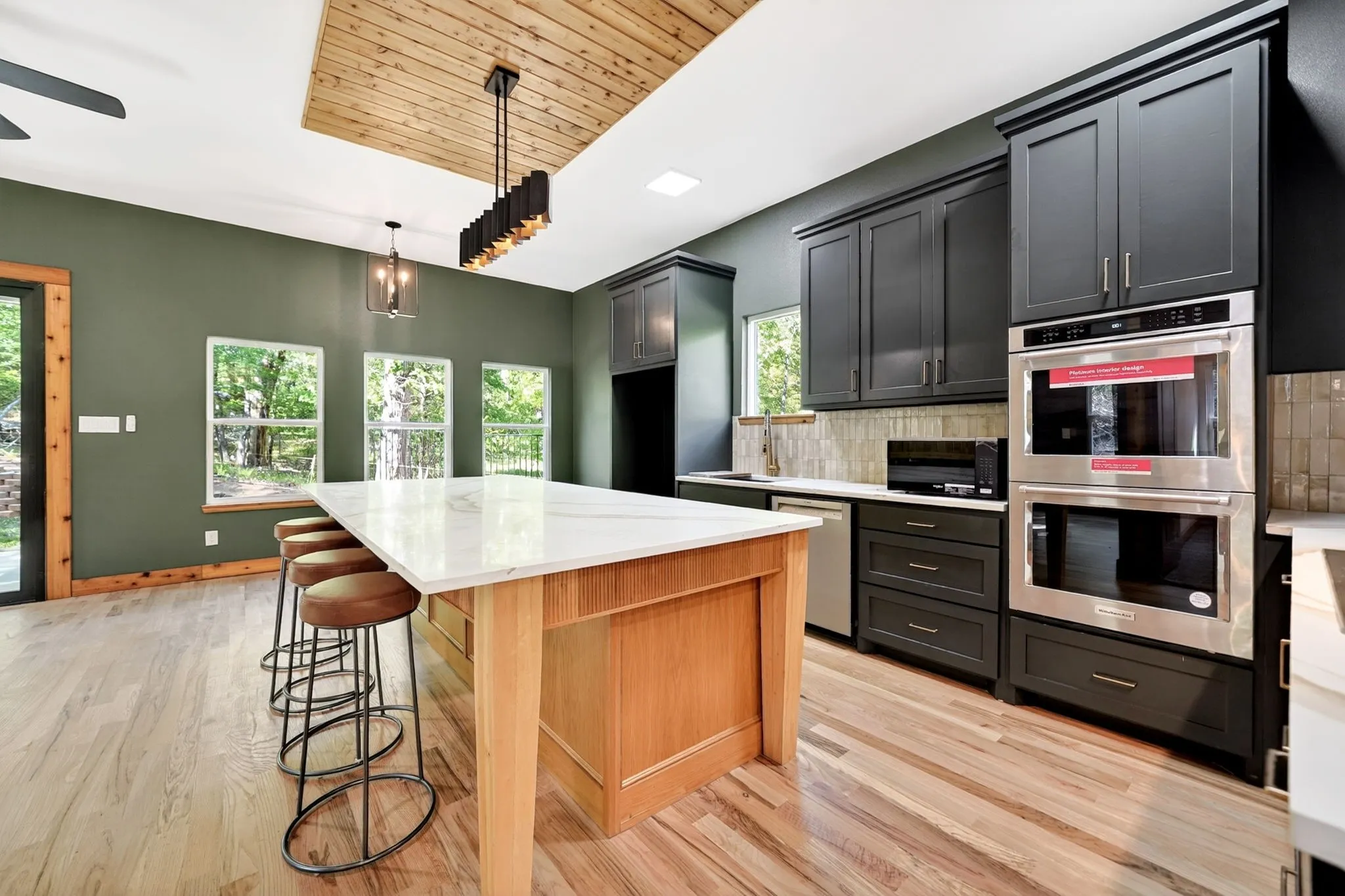 Kitchen featuring a natural-finish wood center island with a stone countertop, dark cabinetry, stainless steel double wall ovens, wood-finish flooring, and a recessed ceiling accent with plank wood detailing