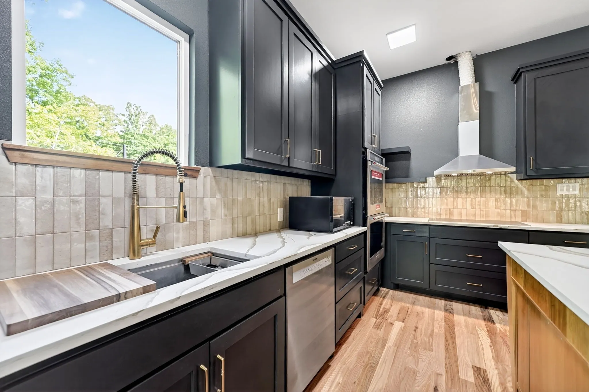 Kitchen featuring dark cabinetry, stone-surface countertops, textured vertical tile backsplash, stainless steel appliances, and wood-finish flooring