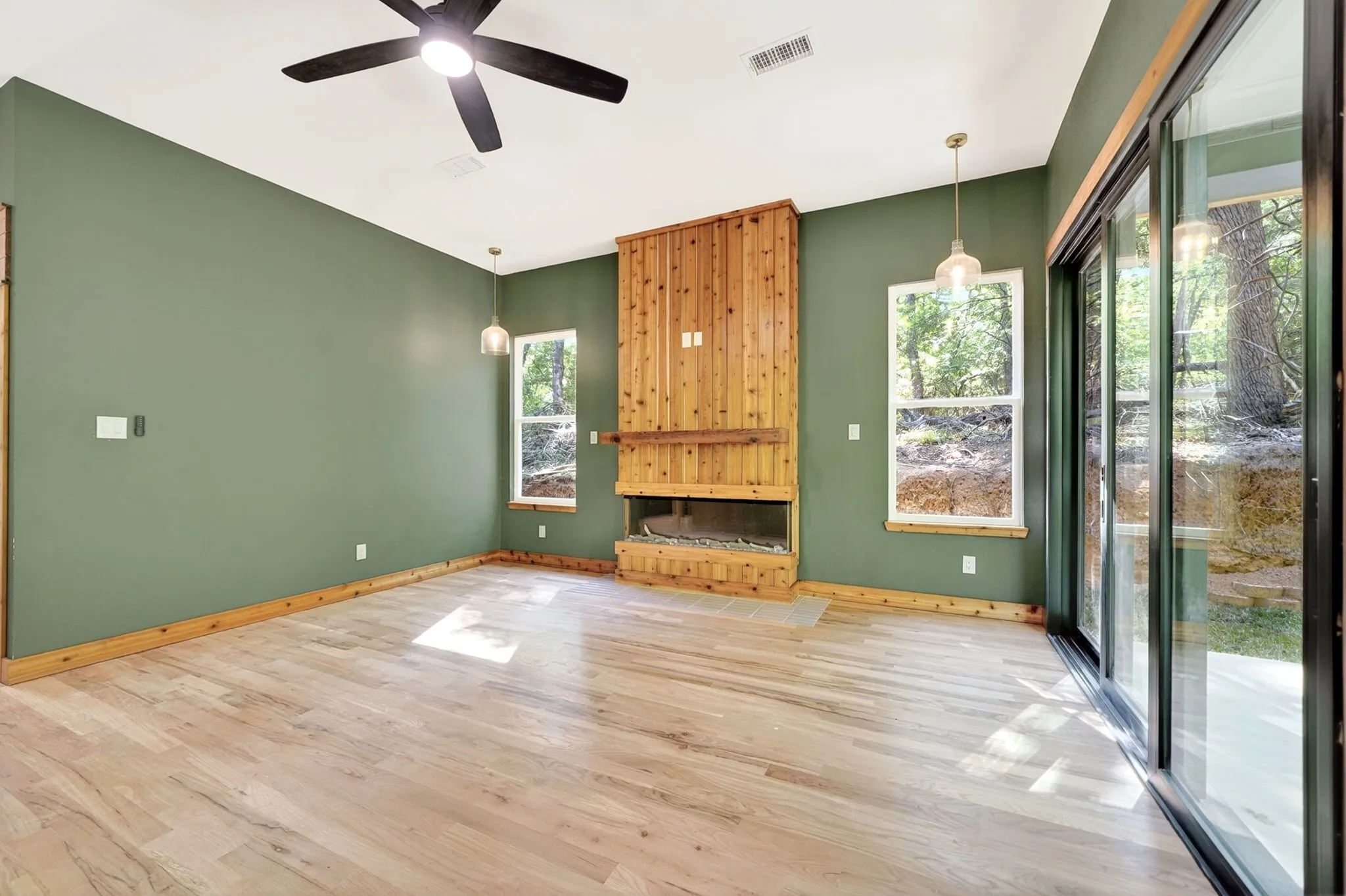Living area featuring wood-finish flooring, a floor-to-ceiling wood-clad fireplace, integrated ceiling fan, and sliding glass doors