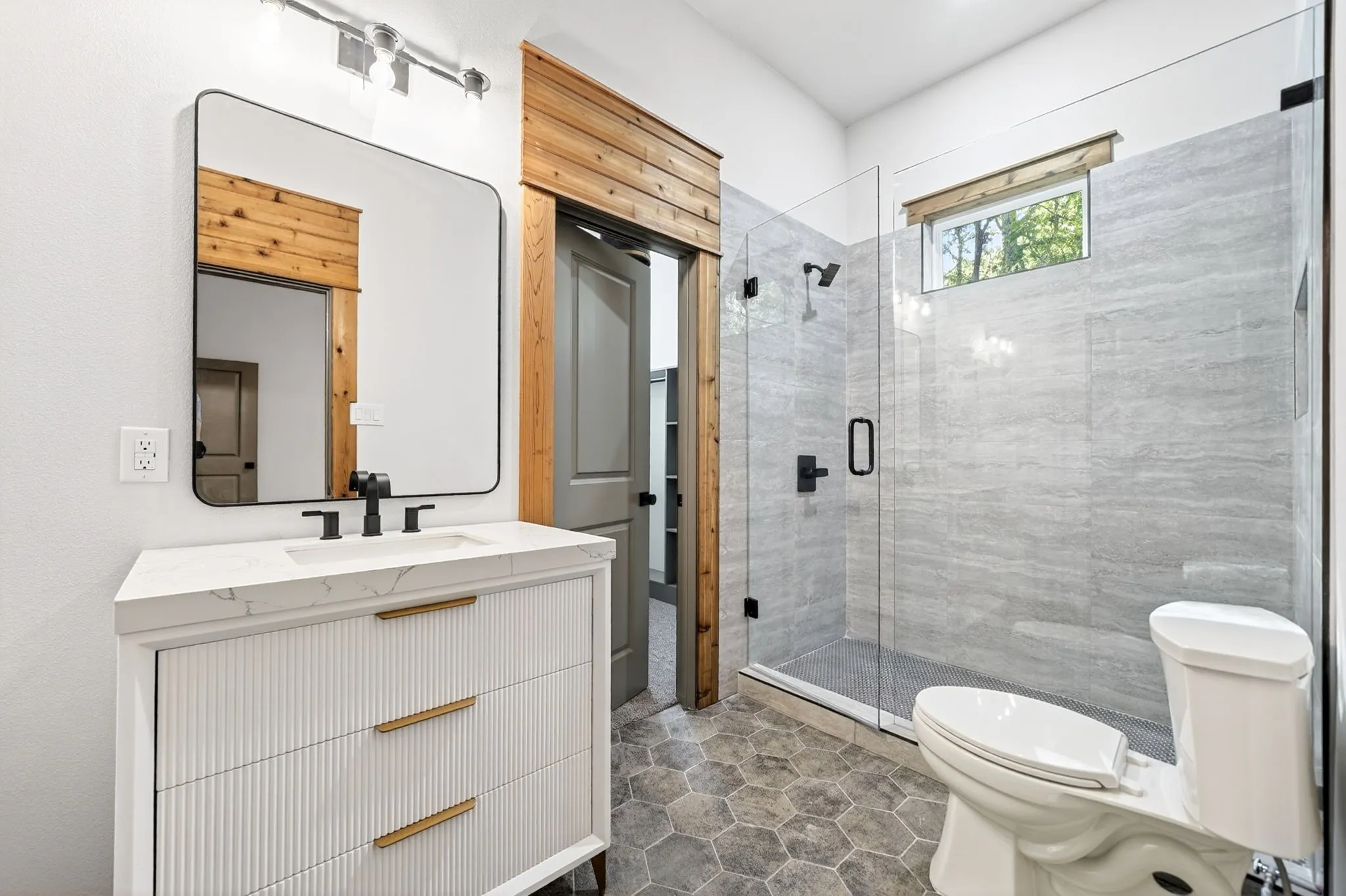 Bathroom featuring a fluted vanity with a stone countertop, walk-in shower with floor-to-ceiling tile, frameless glass enclosure, matte black fixtures, and hexagonal floor tile