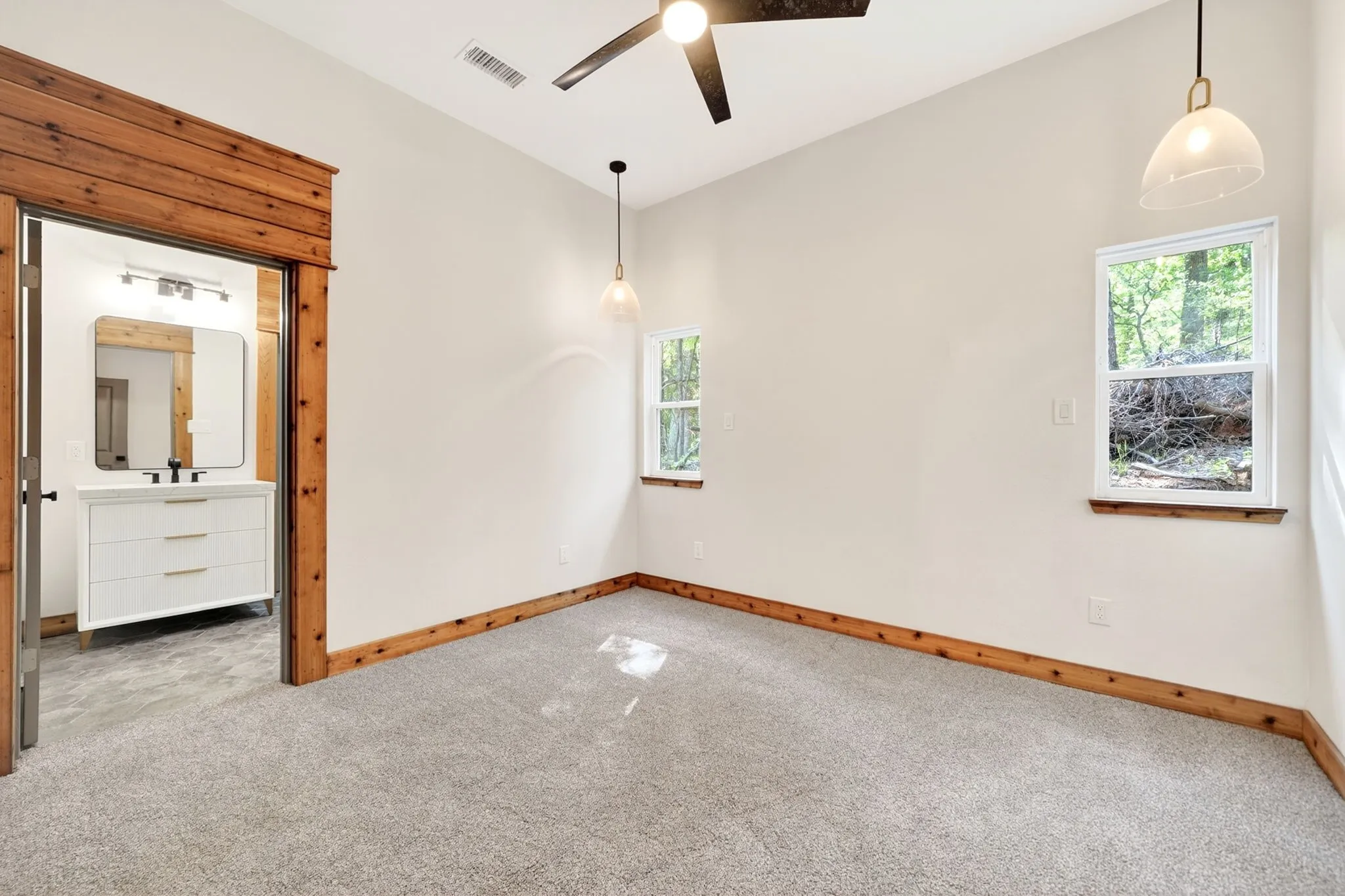 Interior space featuring wood trim accents, neutral wall-to-wall carpeting, dual hanging pendant light fixtures, and a matte black ceiling fan