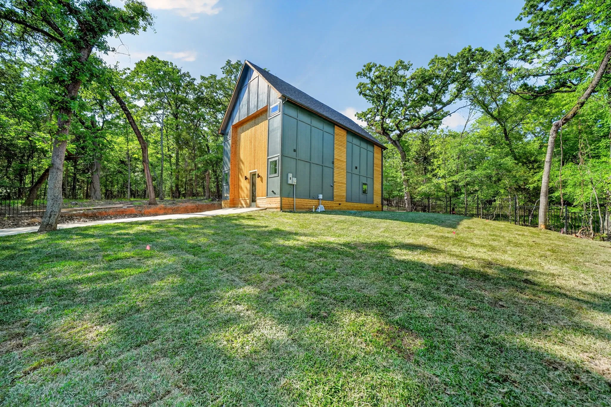 Modern architectural exterior featuring metal panel siding, vertical wood-finish siding, a steep pitched roofline, and expansive surrounding woodland