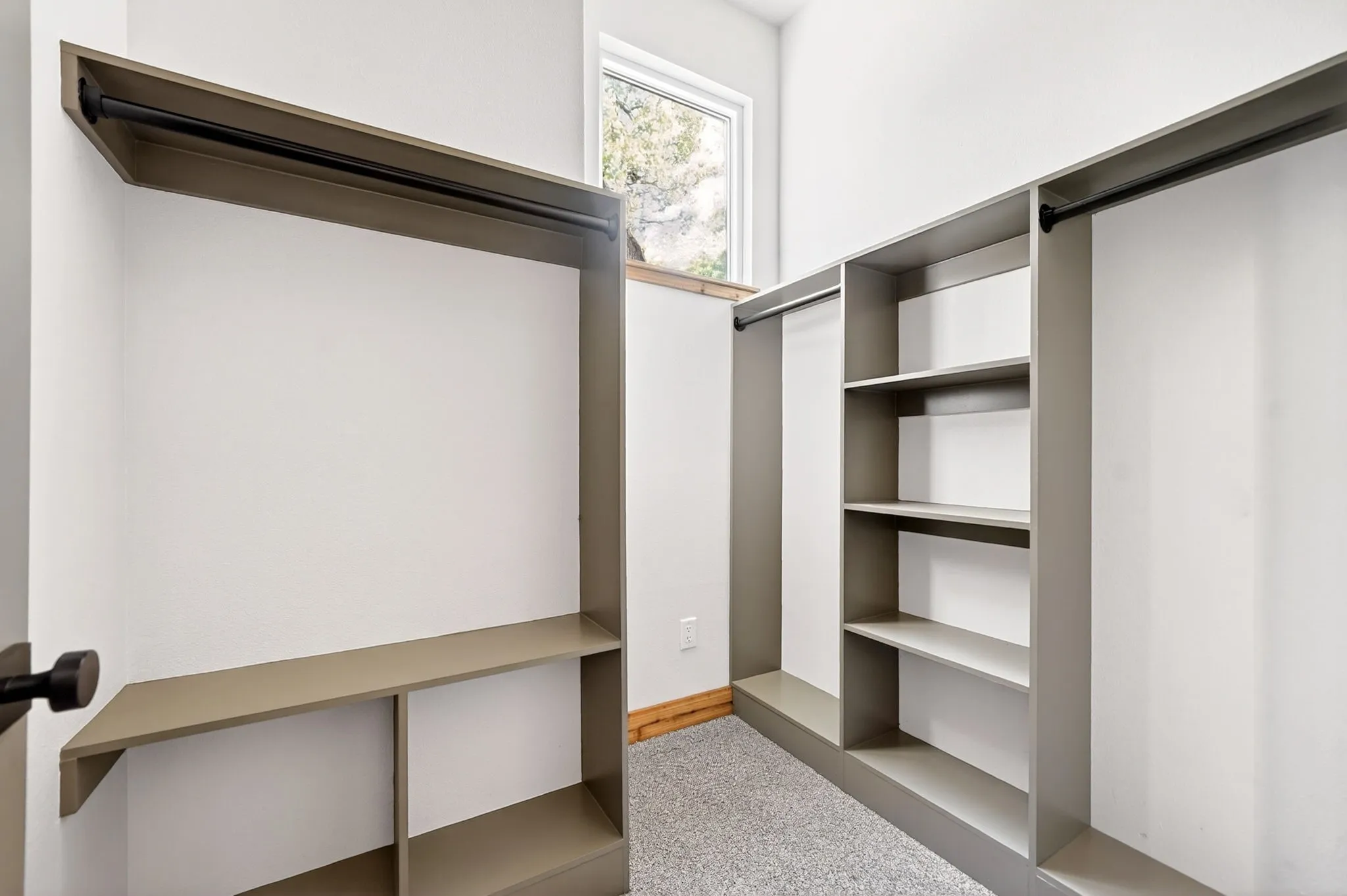 Custom storage system featuring neutral-toned cabinetry, built-in shelving, integrated garment rods, and a window allowing for natural light