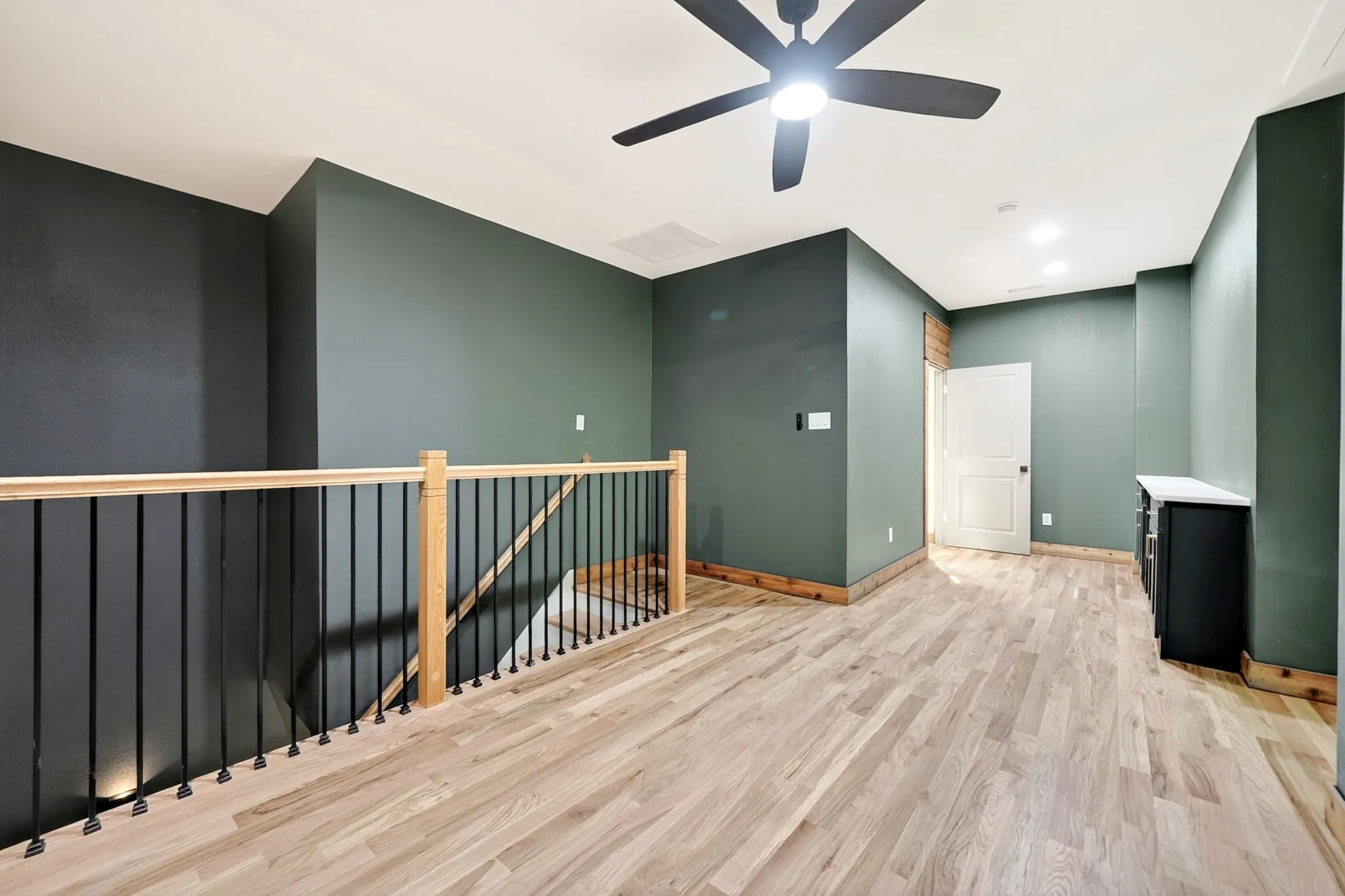 Open loft space featuring wood-finish flooring, a wood and metal balustrade, recessed lighting, a modern ceiling fan, and built-in cabinetry