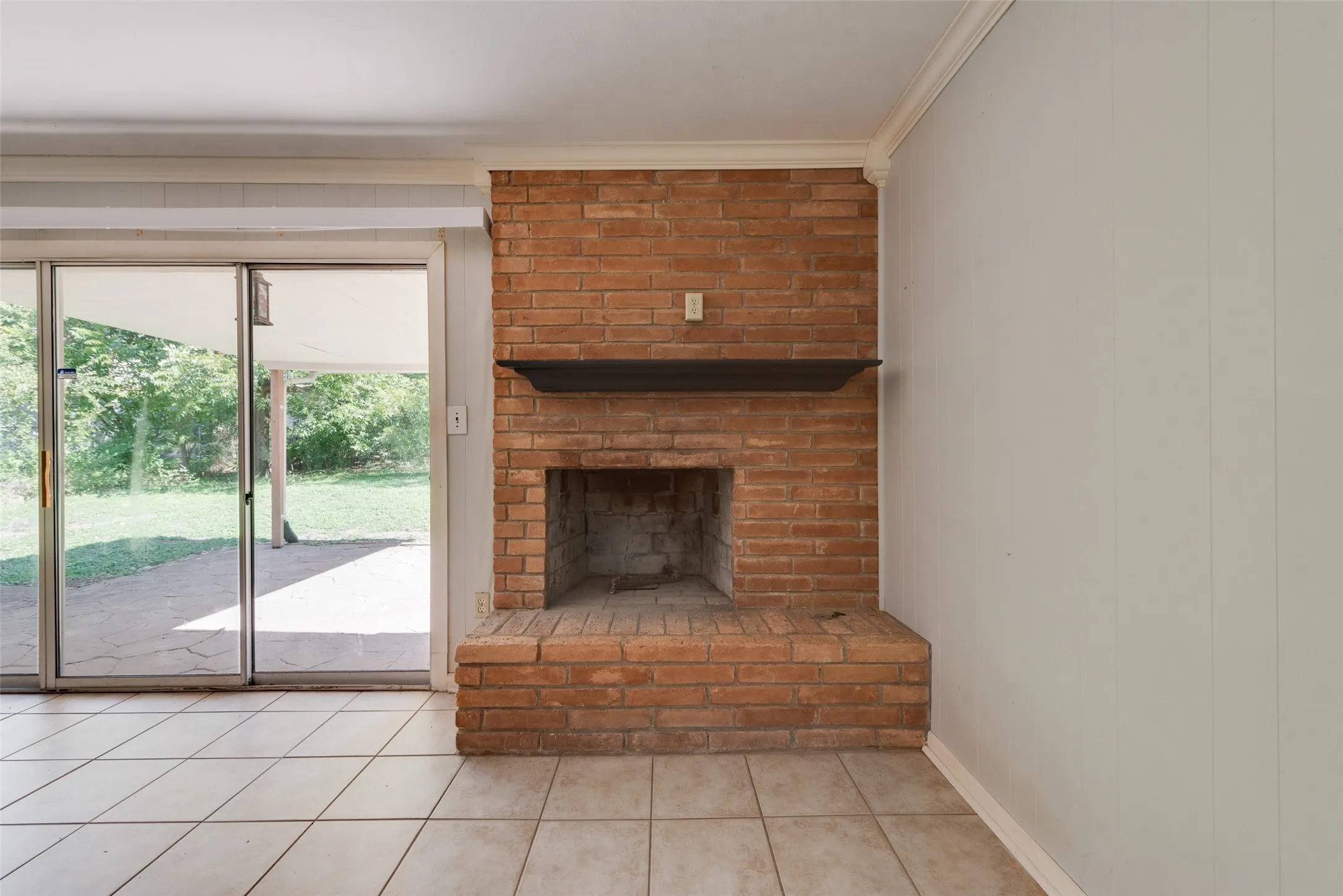Full-height brick fireplace with a raised hearth and dark wood-finish mantel, ceramic tile flooring, and floor-to-ceiling sliding glass doors