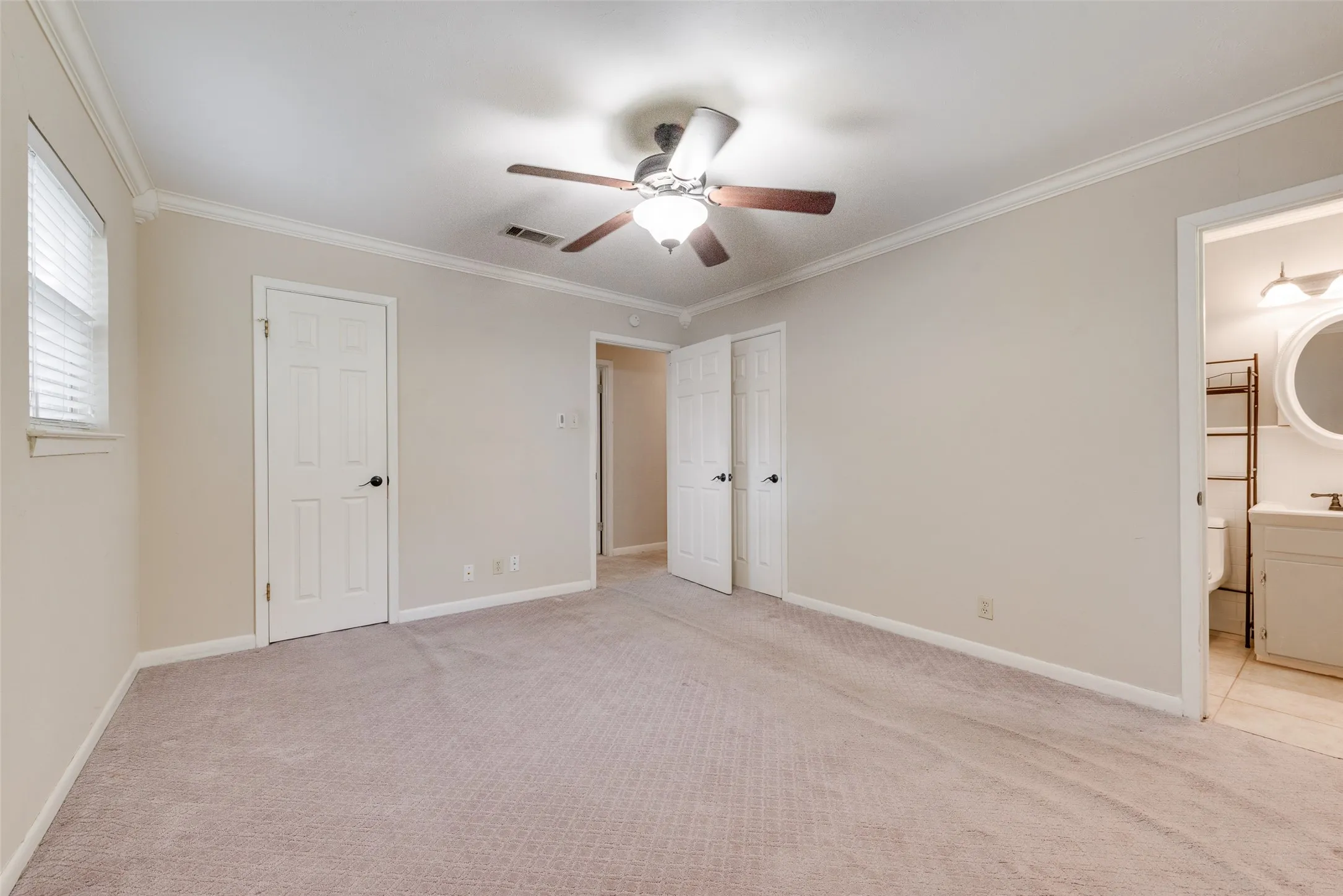Room featuring neutral-toned carpeting, crown molding, a central ceiling fan with integrated lighting, and multiple interior doors