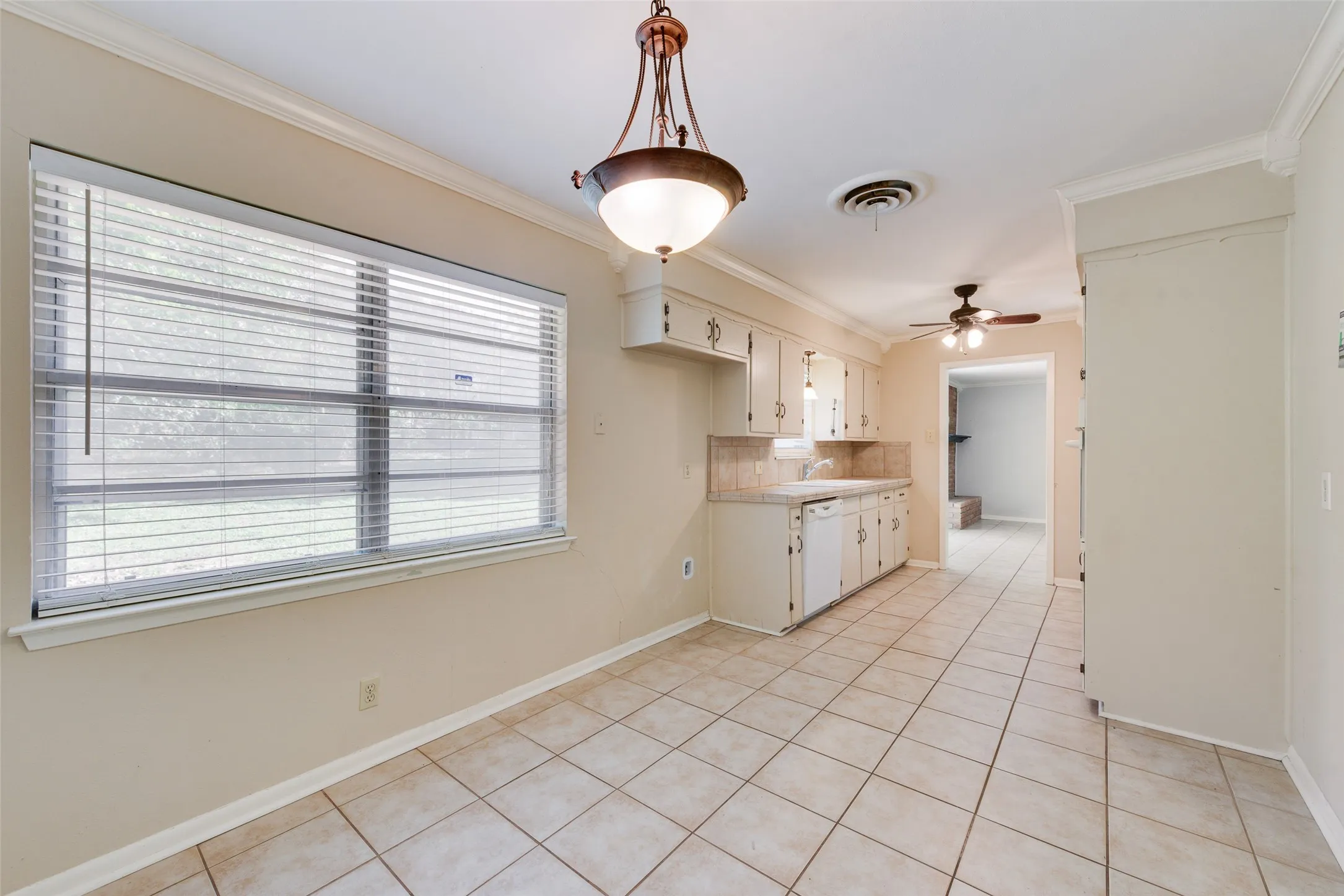 Ceramic tile flooring, large-format window with horizontal blinds, neutral cabinetry, overhead pendant lighting, and crown molding