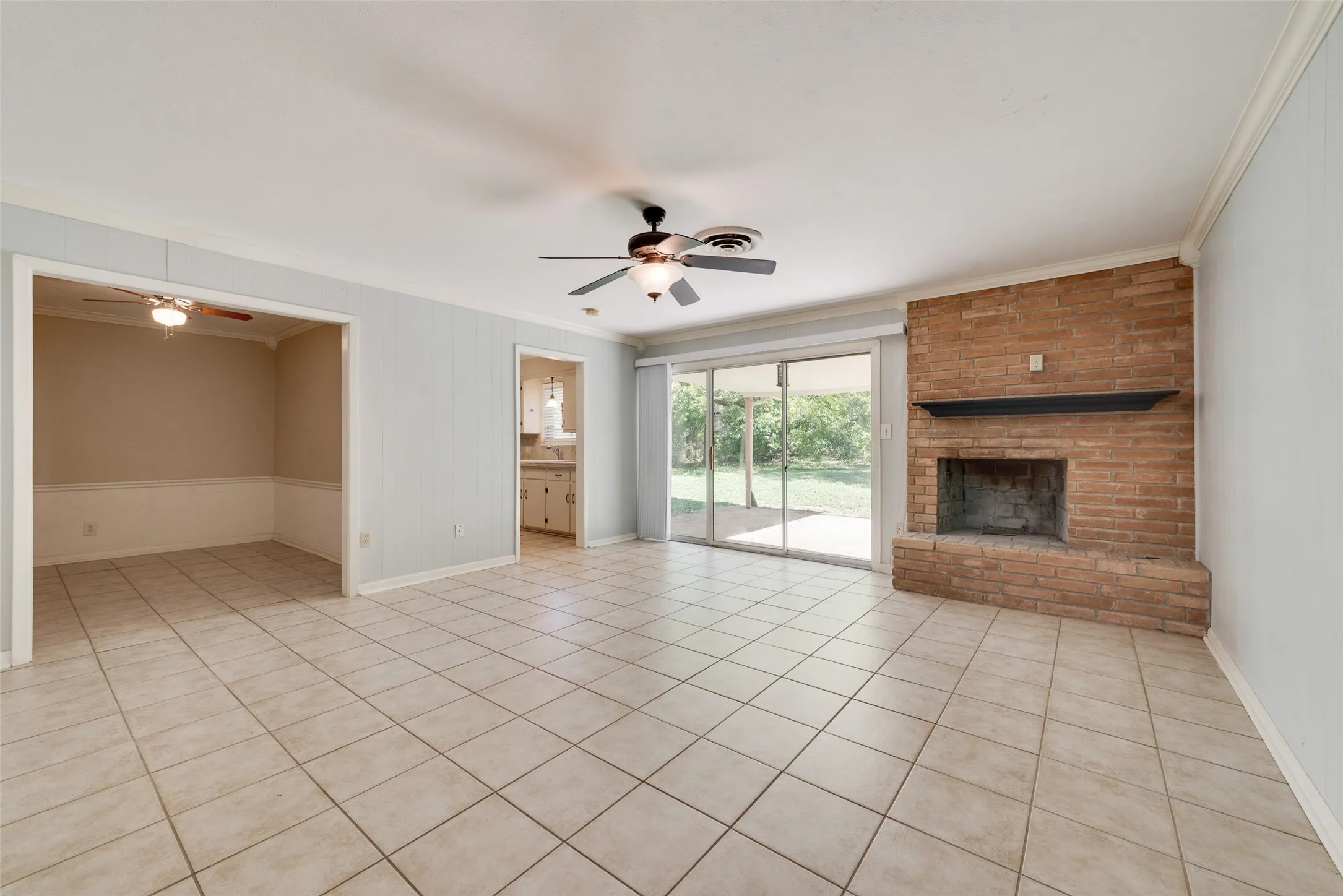 Living area featuring tile flooring, floor-to-ceiling masonry fireplace, black mantel, ceiling fan, and sliding glass doors