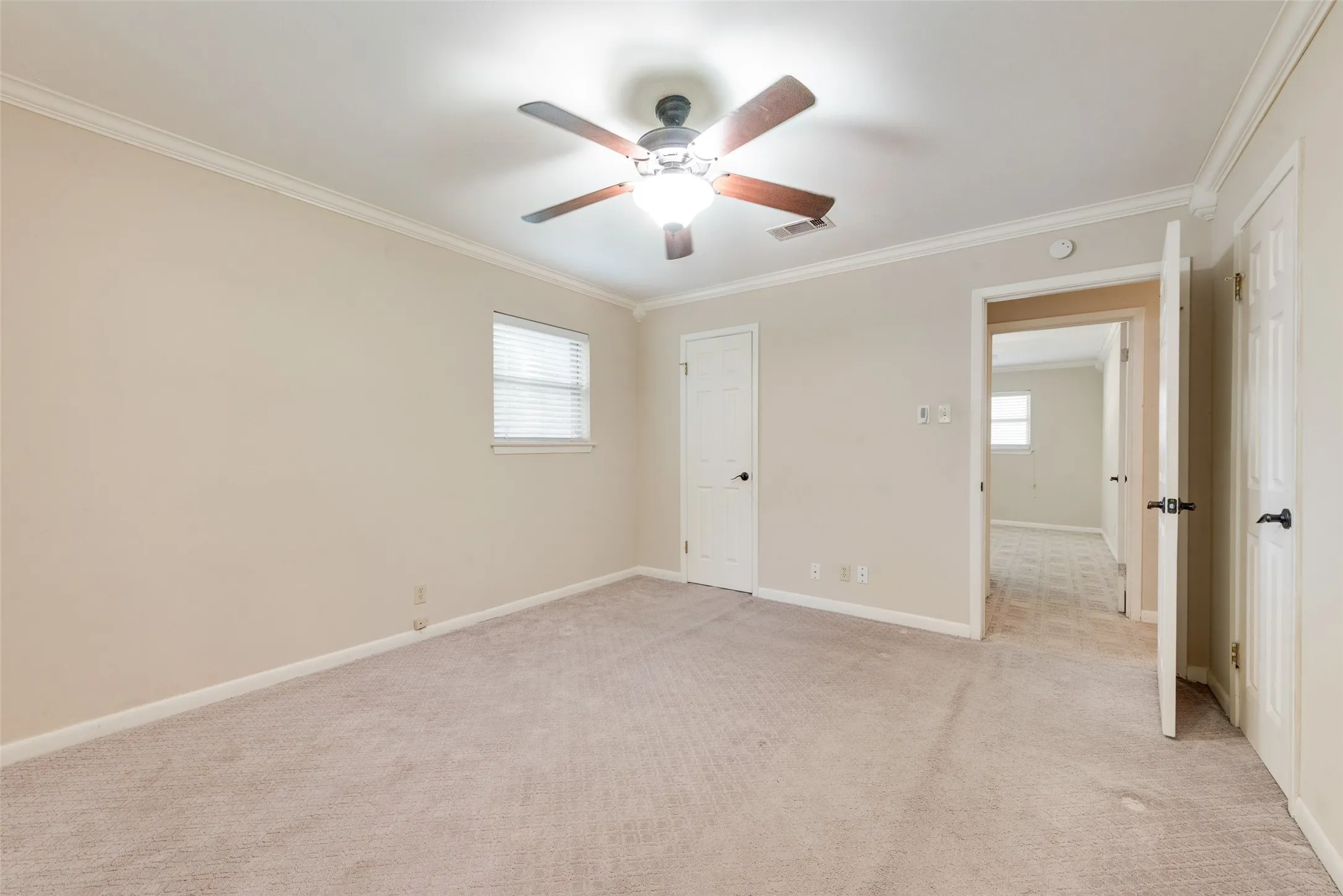 Room interior featuring neutral wall paint, carpeted flooring, crown molding, and a ceiling fan with integrated lighting