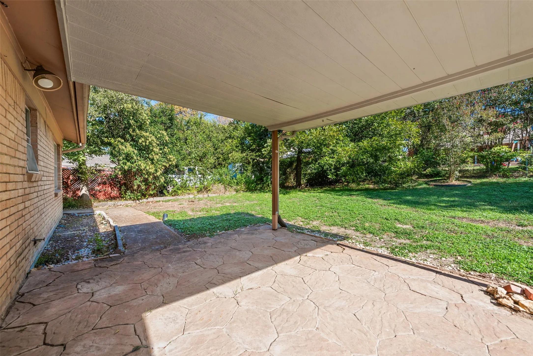 Covered patio featuring a flagstone floor, brick exterior wall, and integrated overhead lighting, opening to a grass lawn