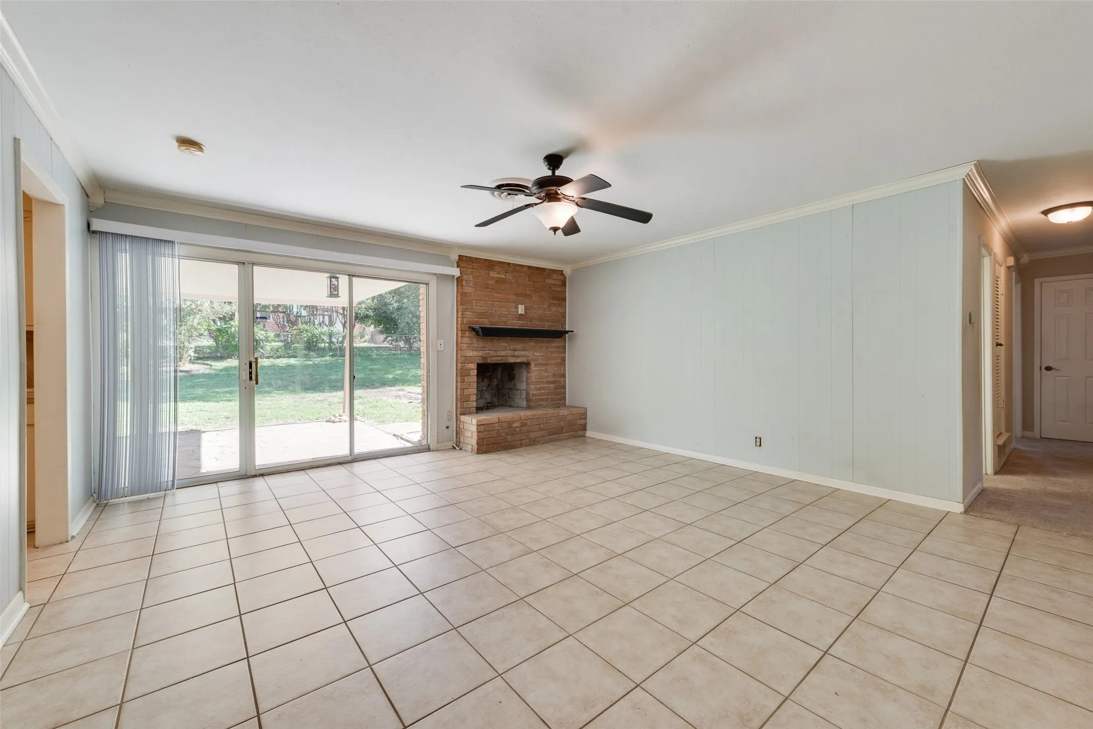 Living area featuring tile flooring, floor-to-ceiling brick fireplace, sliding glass door, and a ceiling fan