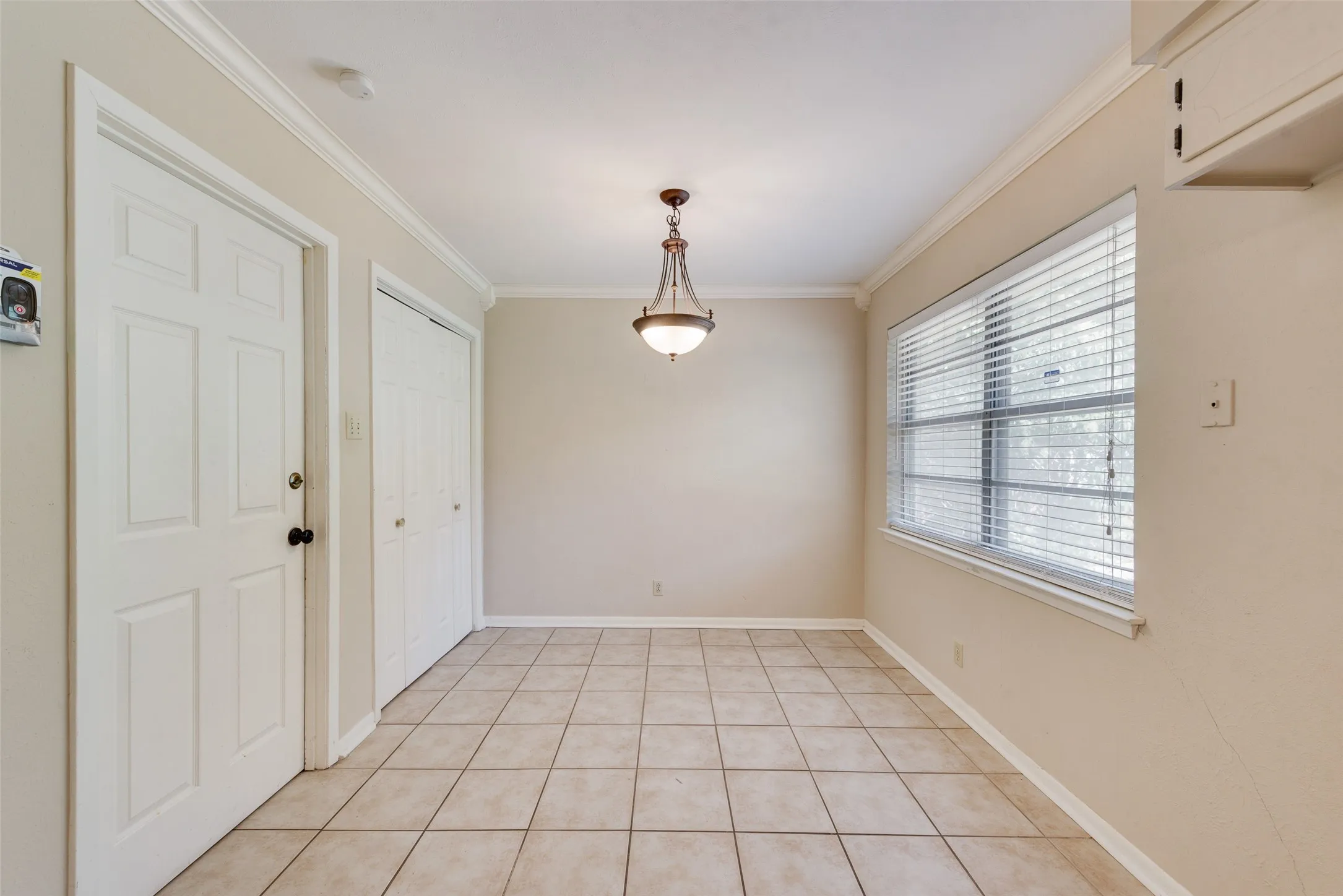 Room featuring neutral-toned tile flooring, crown molding, a central pendant light fixture, horizontal slat blinds, and dual-panel closet doors