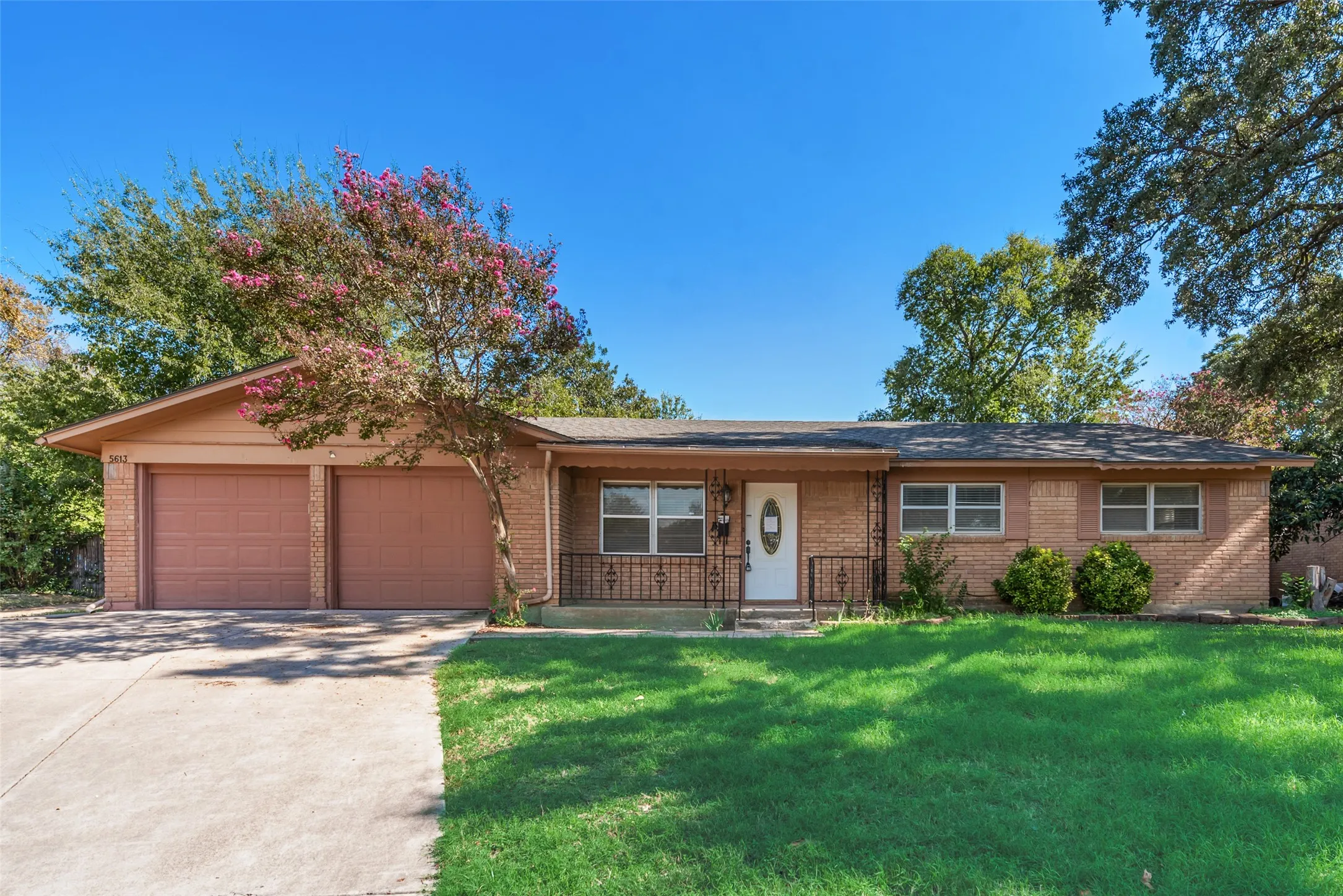 Single-story brick exterior featuring a double-car garage, wrought-iron porch railing, and a concrete driveway