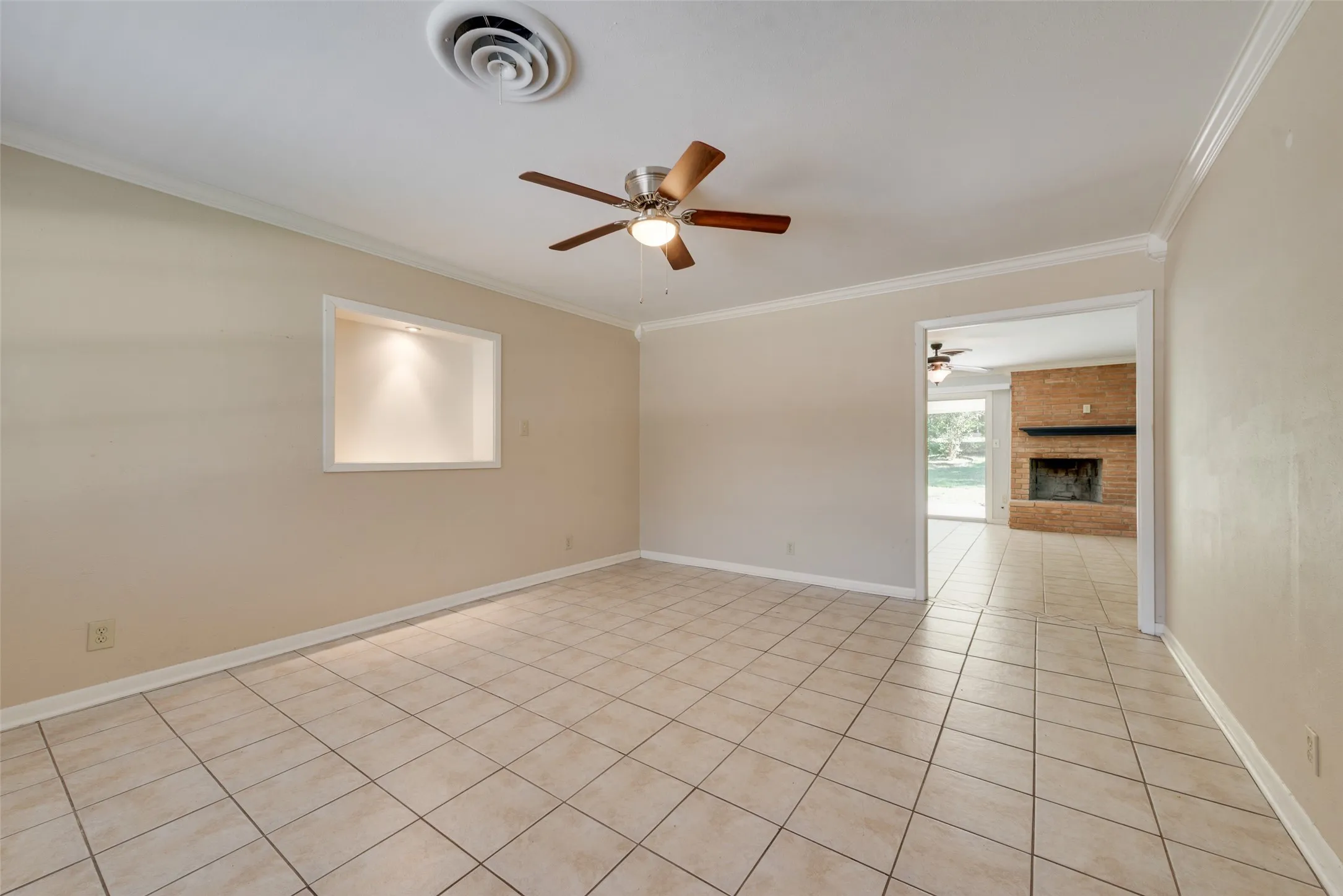 The living room looking into the den featuring large-format ceramic tile flooring, crown molding, a recessed wall niche with accent lighting.