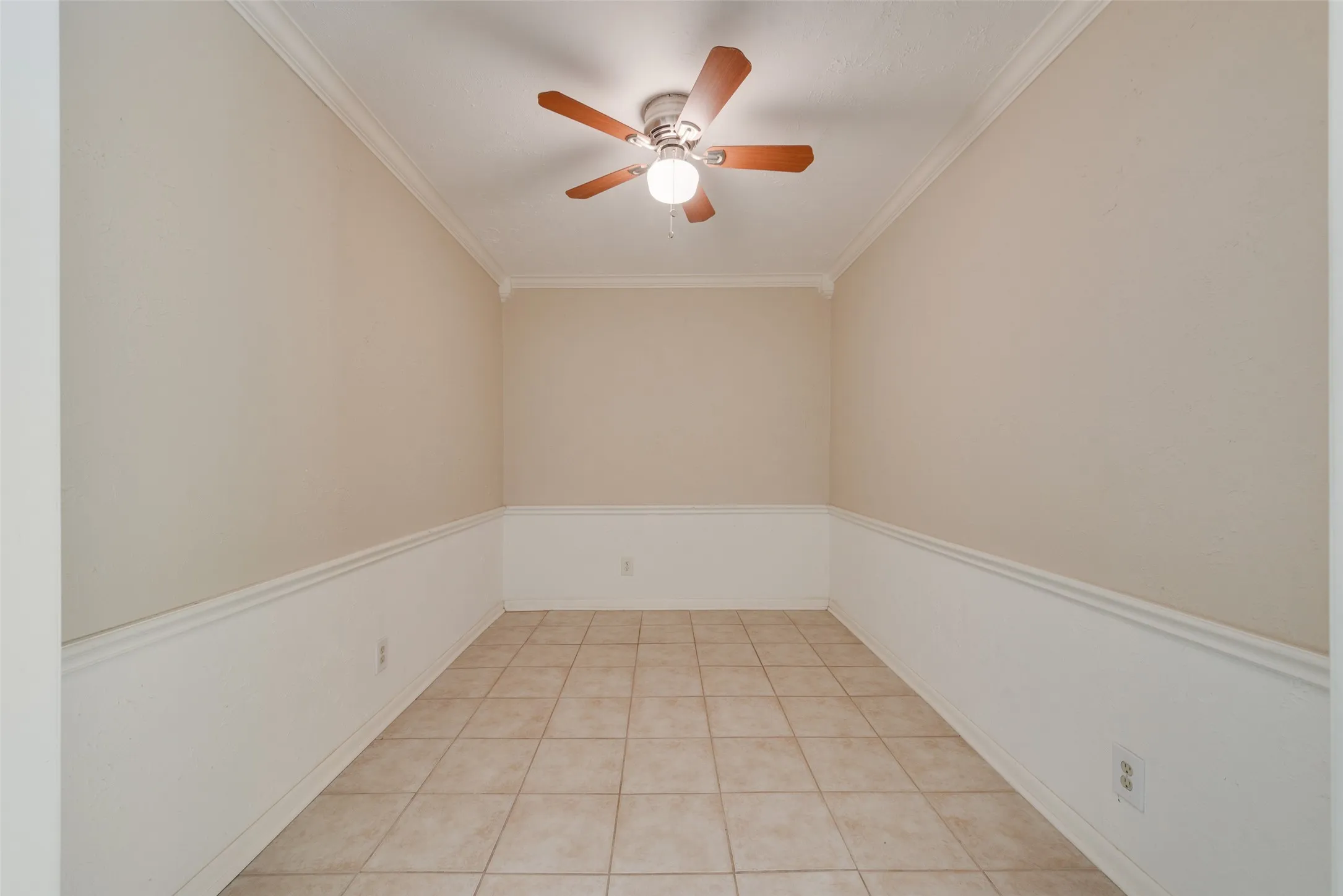 Neutral-toned room featuring tile flooring, white wainscoting with chair rail molding, and a central ceiling fan with integrated lighting